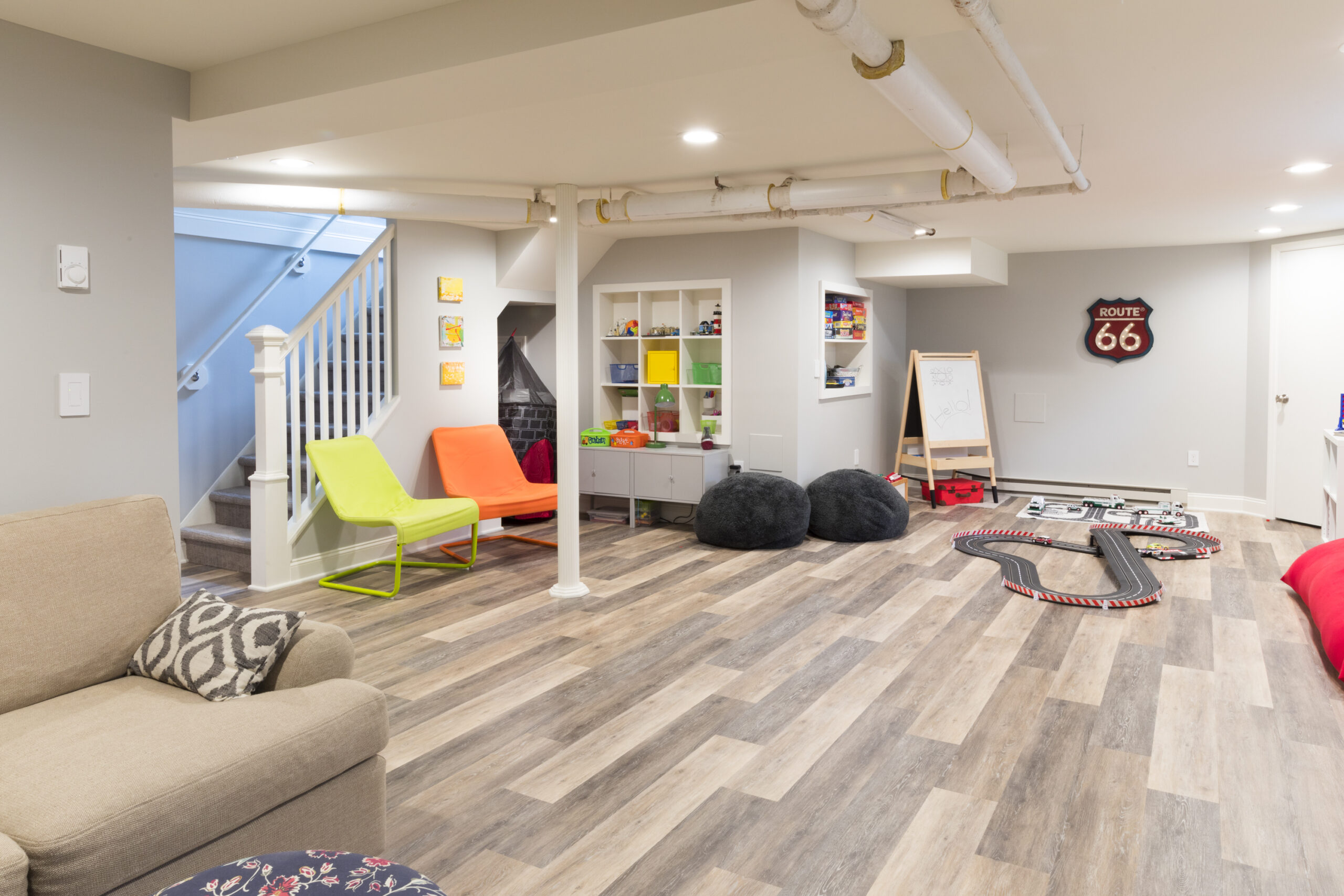 Bergen County basement remodel ideas feature an open family playroom with built-in storage, engineered plank flooring, recessed lights, and exposed pipes.