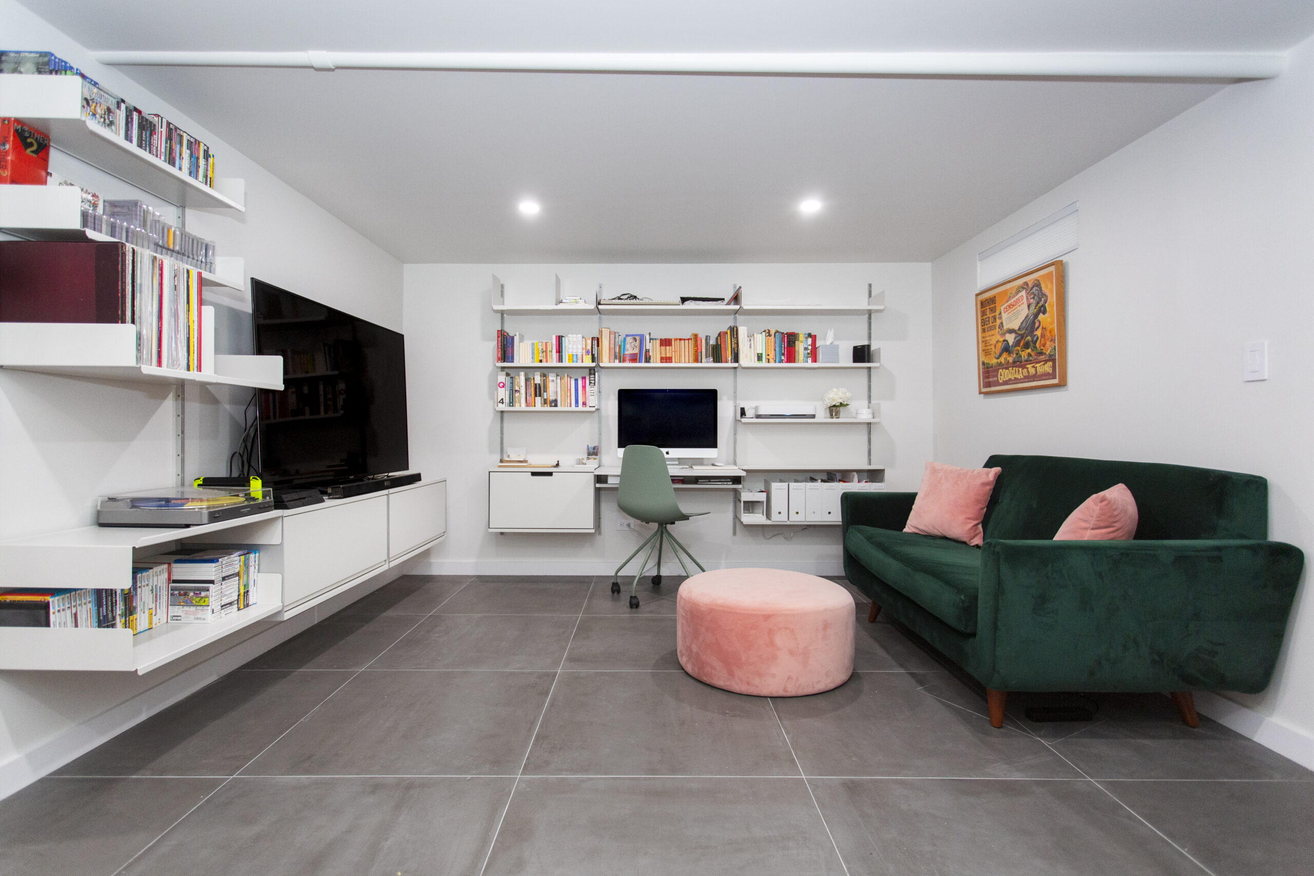 Sunnyside basement remodel ideas feature a flexible living room with wall shelving, a media center, work desk, gray tile floors, and colorful seating.
