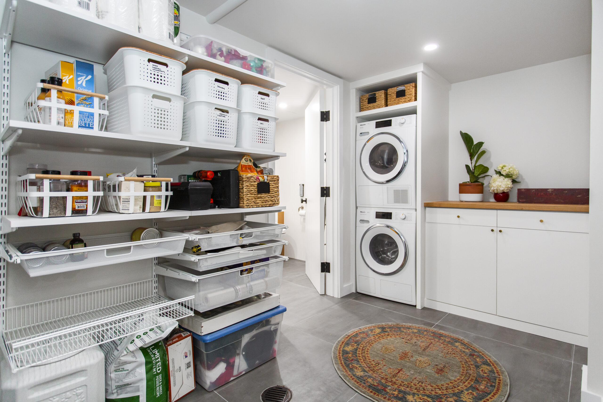 Queens basement remodel combines stacked laundry, custom cabinetry, wood countertop, open shelving, and organized utility storage in one compact space.