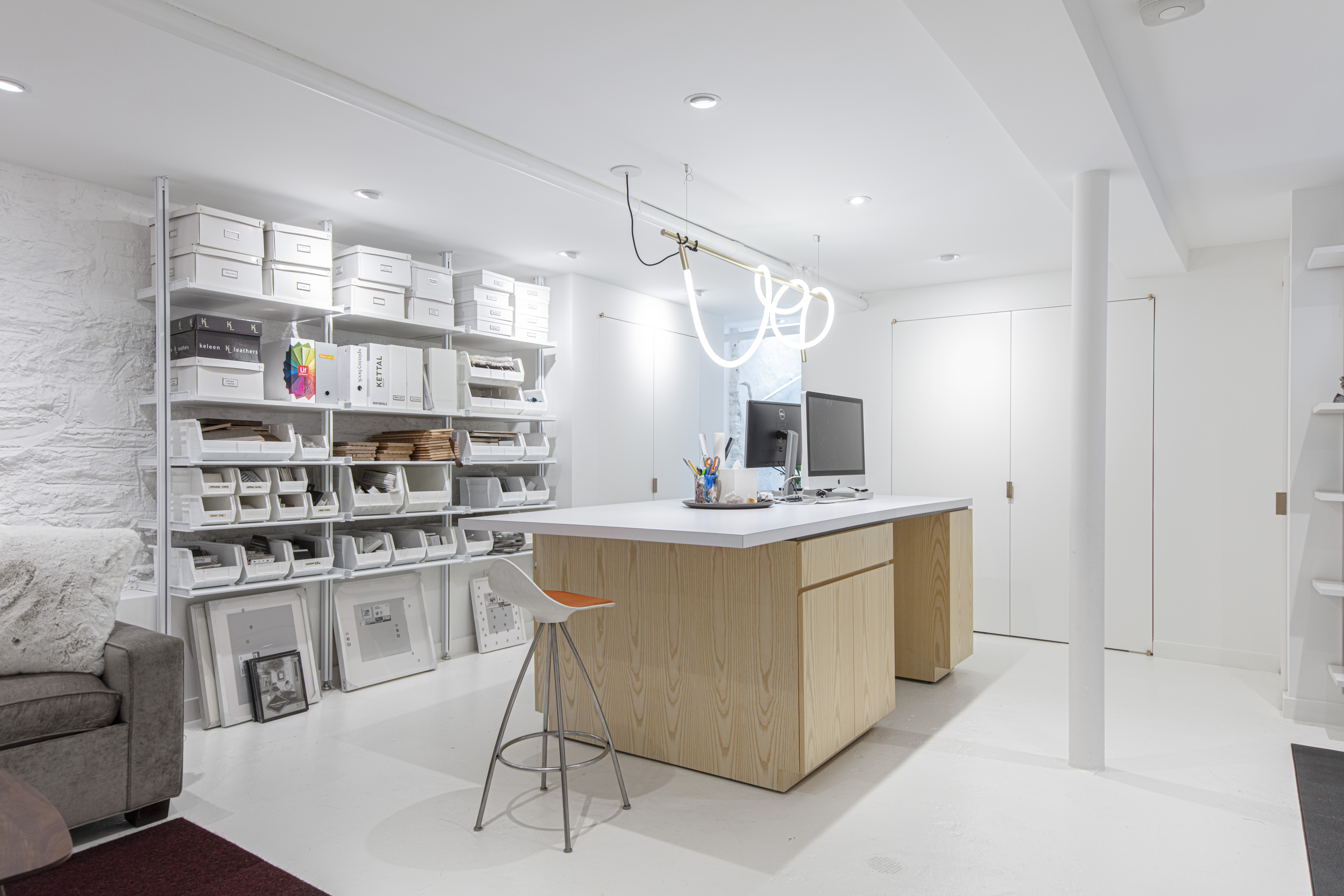 Brooklyn basement home office with a large wood work island, open storage shelves, white epoxy floors, recessed lighting, and concealed storage doors.