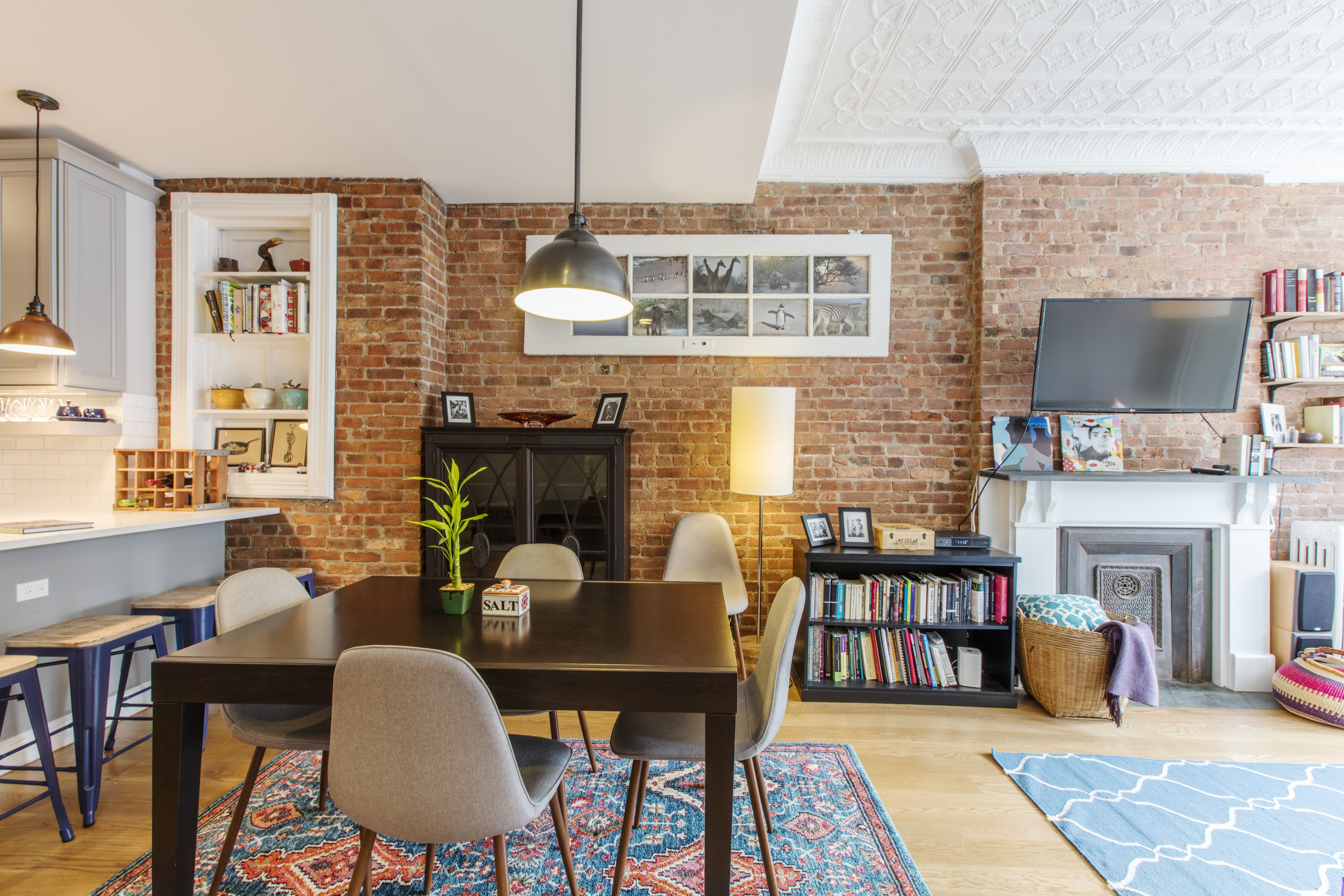 Park Slope home lighting design pairs illuminated dining and kitchen pendants with exposed brick, restored ceiling detail, and open-plan living.