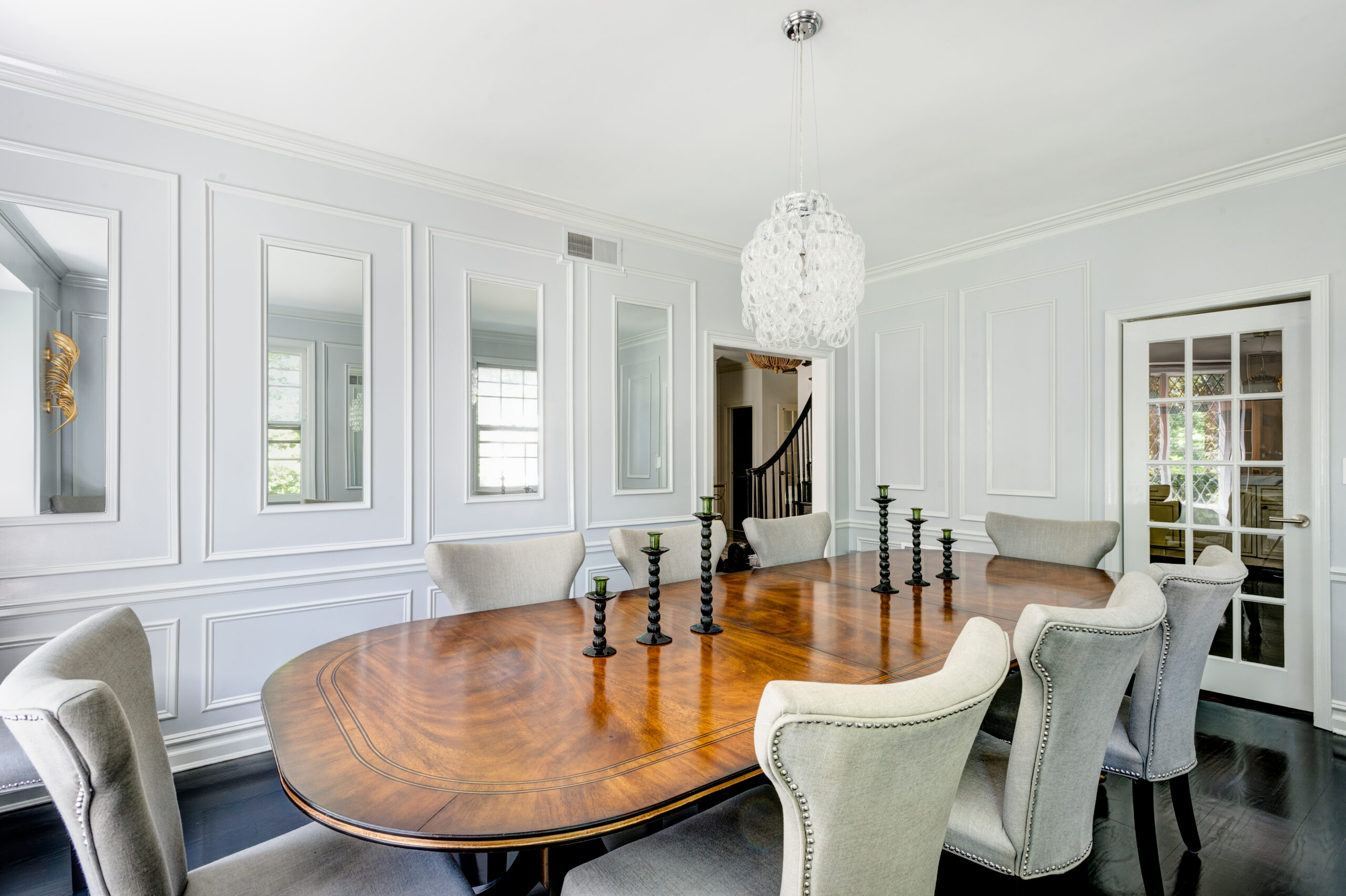 Westchester home lighting design centers a glass pendant above a large wood dining table, with paneled walls, mirrors, and dark hardwood floors.