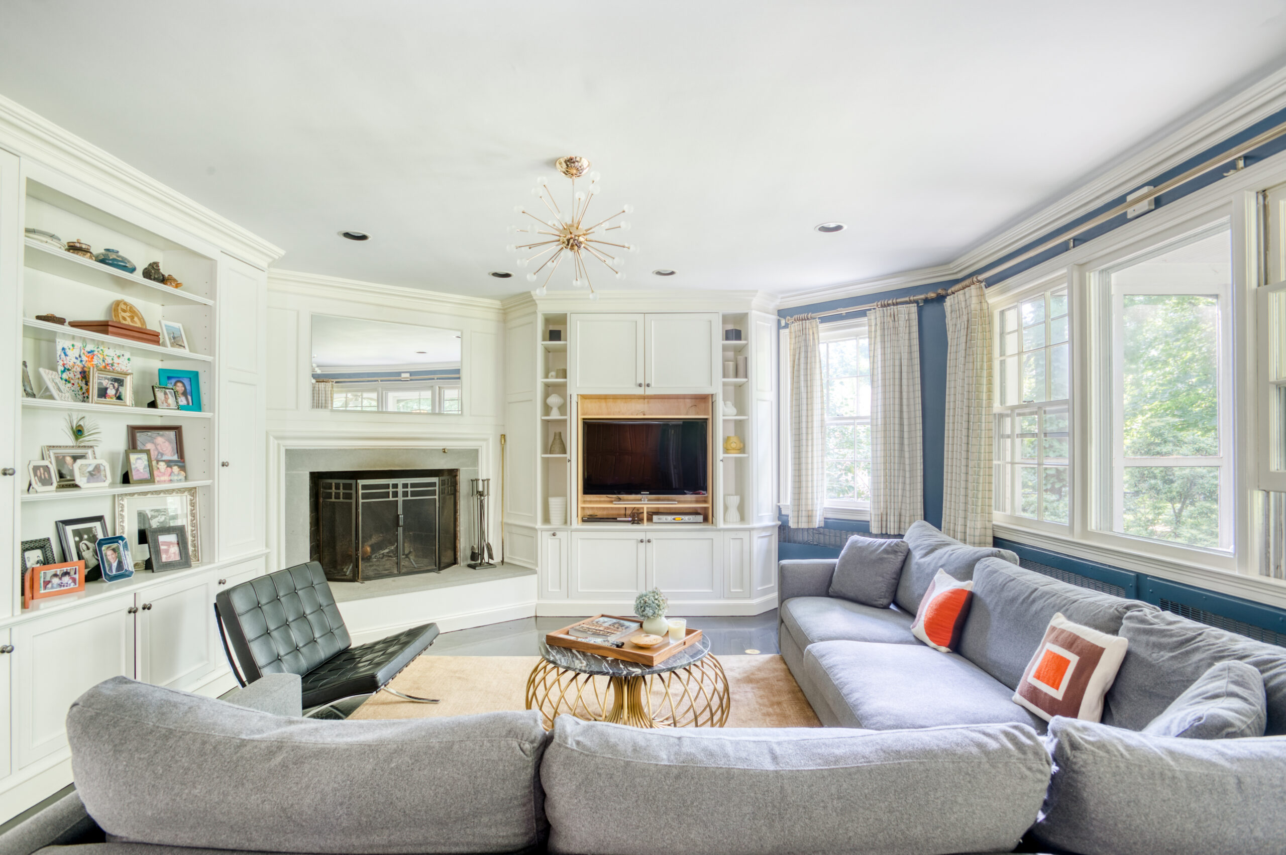 Westchester home lighting design combines a Sputnik chandelier, recessed lights, large windows, white built-ins, and a blue-accented living room.