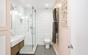 A modern bathroom with a glass shower door, white subway tiles, and bold patterned floor tiles.