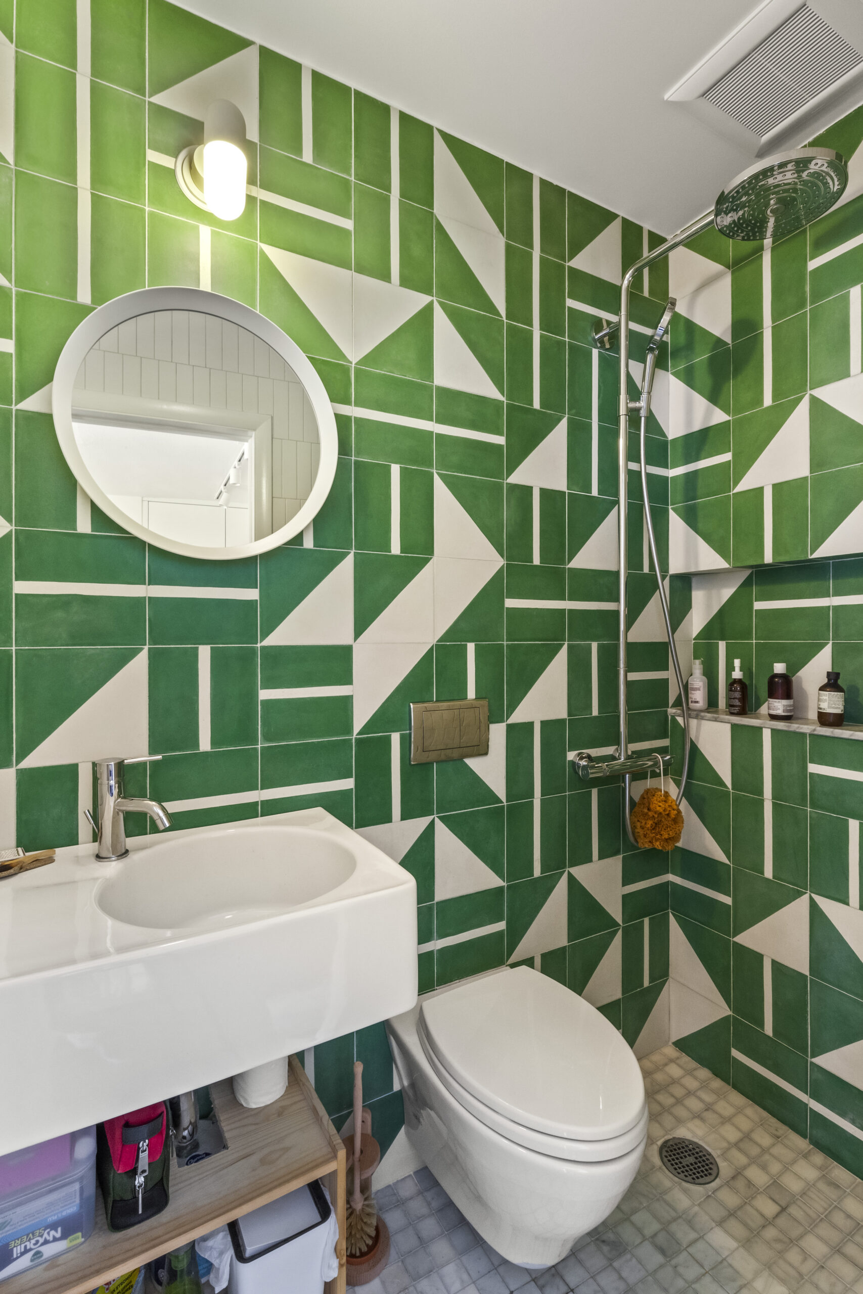 A renovated bath with green and white cement tiles, white sink and toilet, and circular mirror