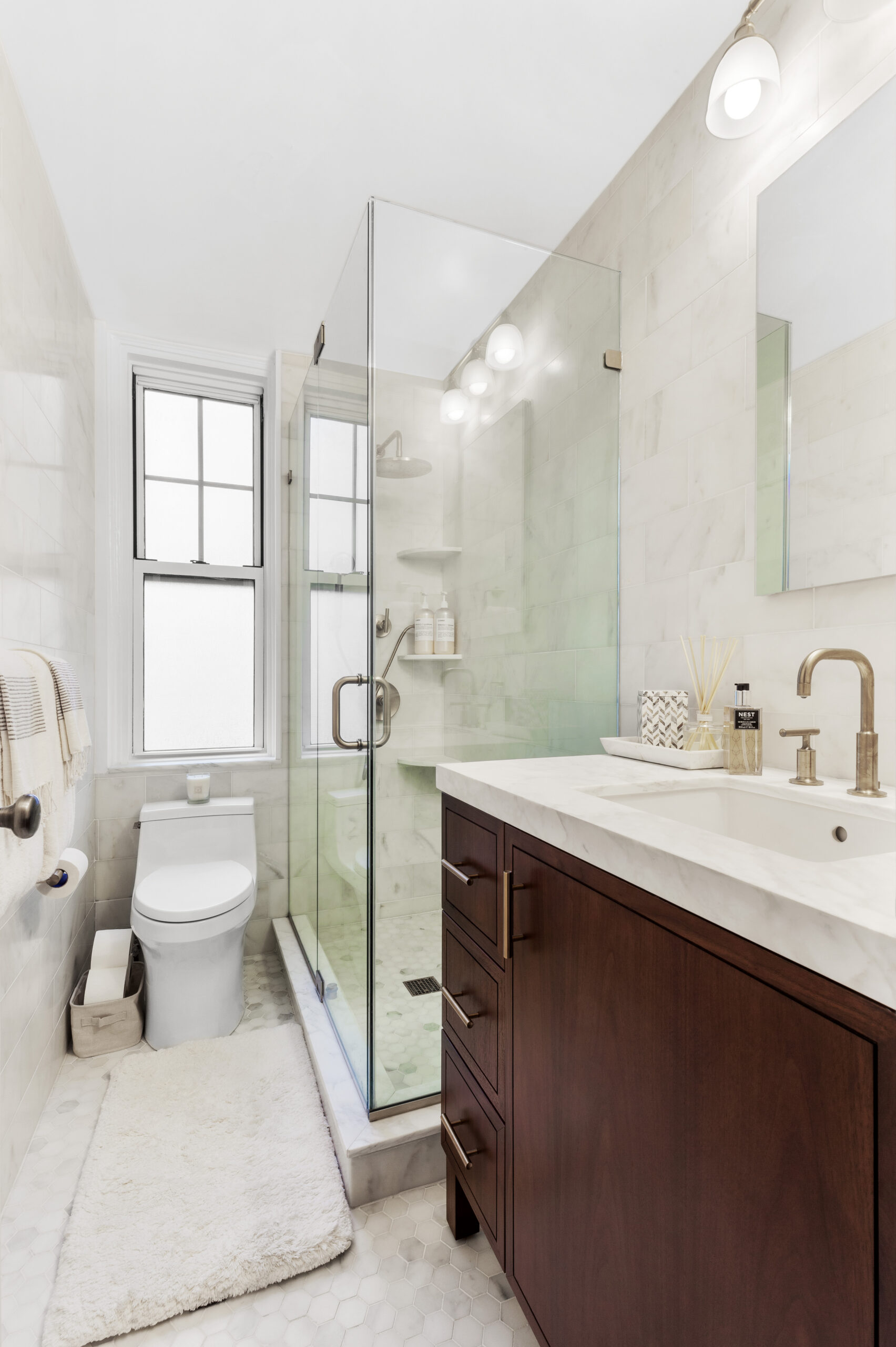 A renovated bathroom featuring Calacatta Gold marble counter, hex mosaic floor, and glass door shower