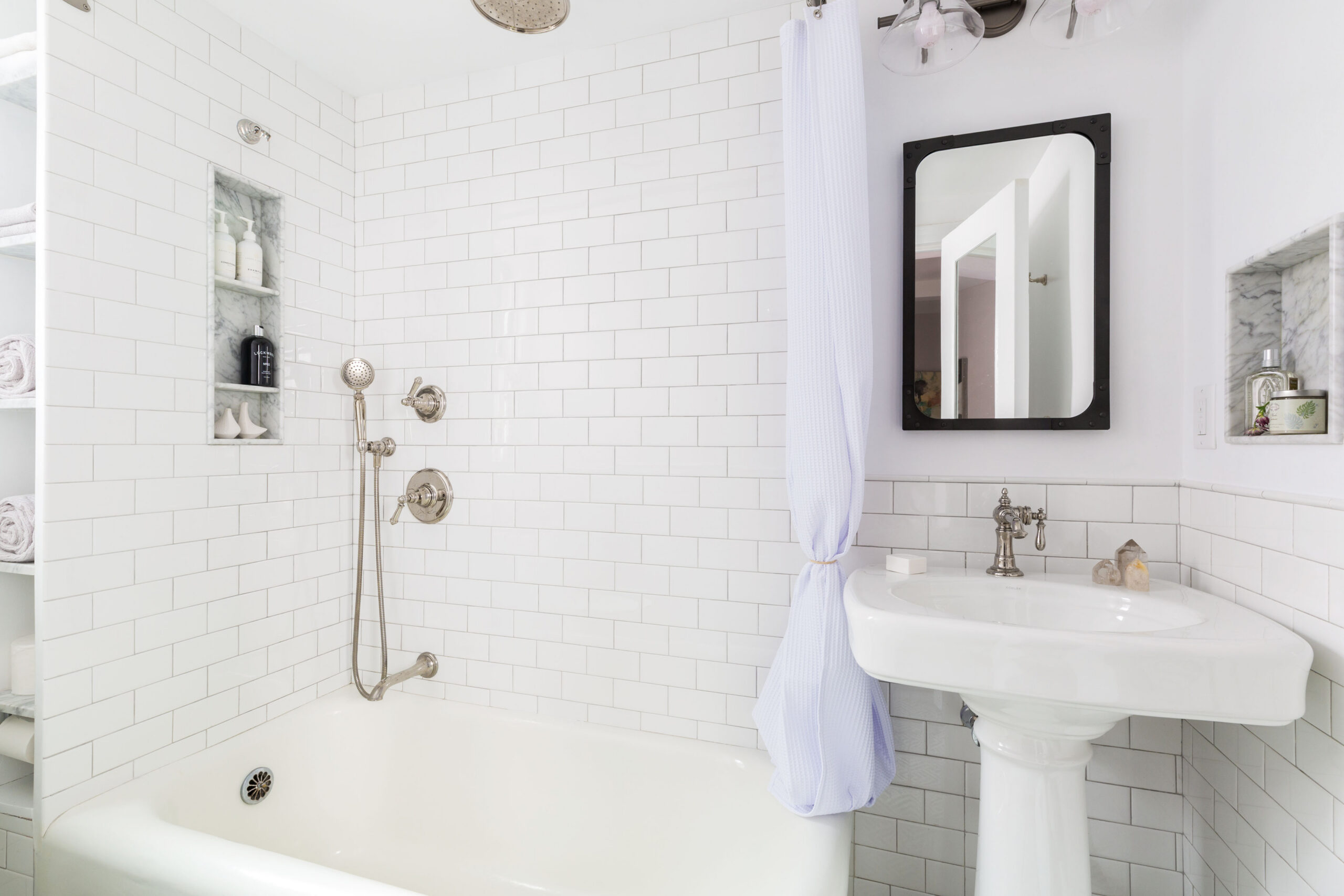 A renovated bath with white subway wall tile, shower curtain, tub, and mirror