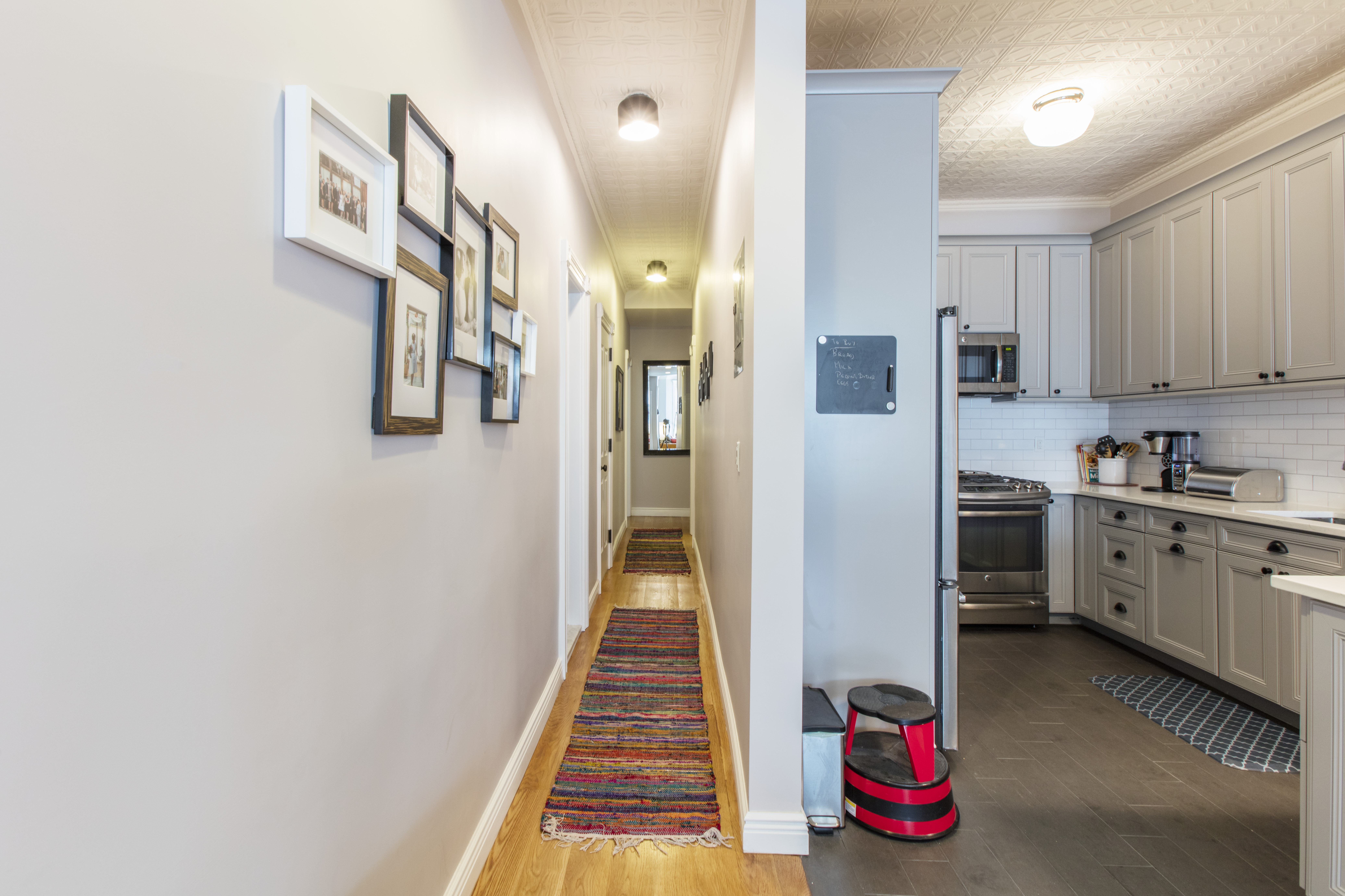 Brooklyn brownstone remodel with an oak-floored hallway opening to a gray kitchen with paneled cabinets, subway tile, and preserved tin ceilings.