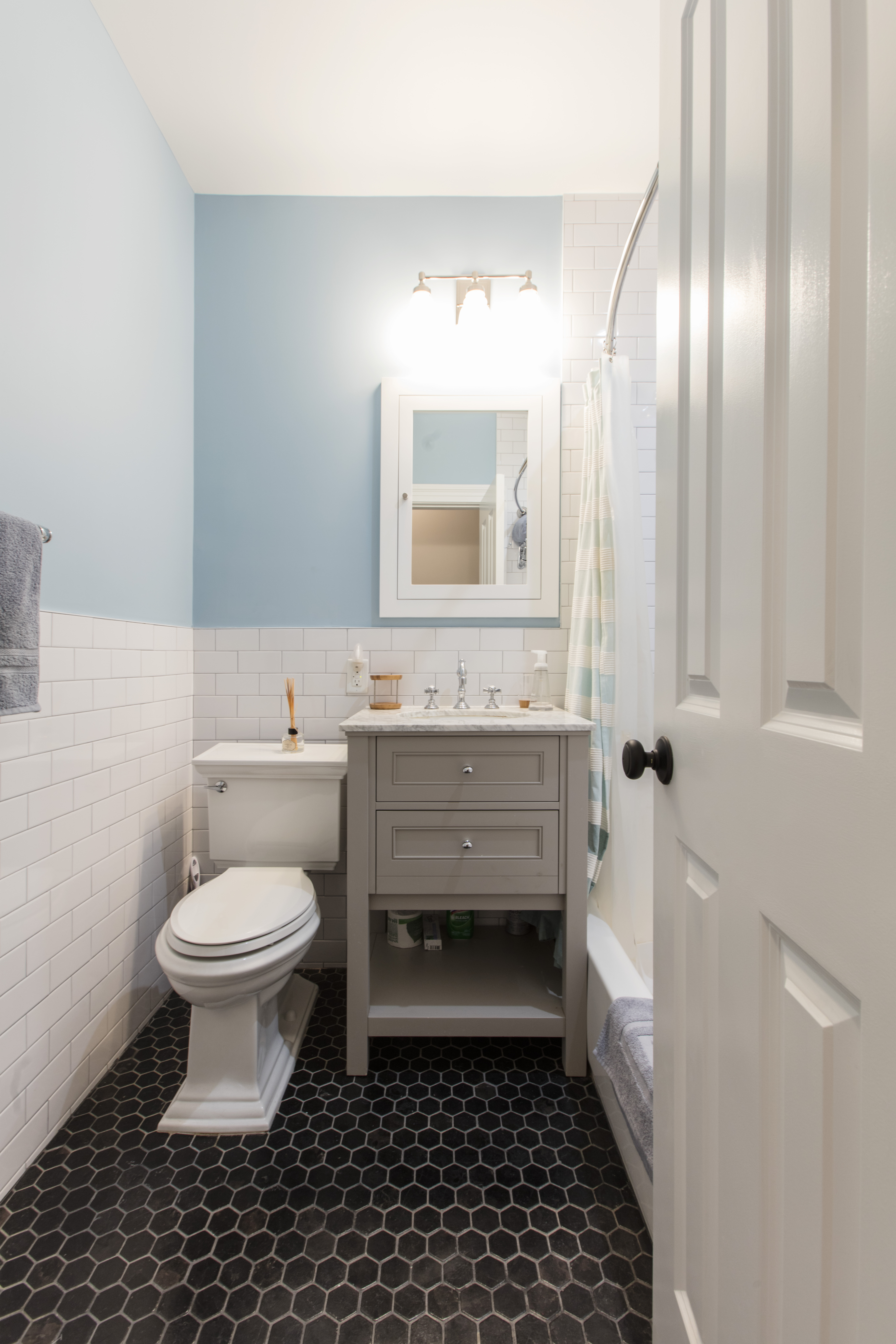 Brooklyn brownstone remodel bathroom with black hex floor tile, gray vanity, white subway tile, blue walls, framed mirror, and a tub and shower.