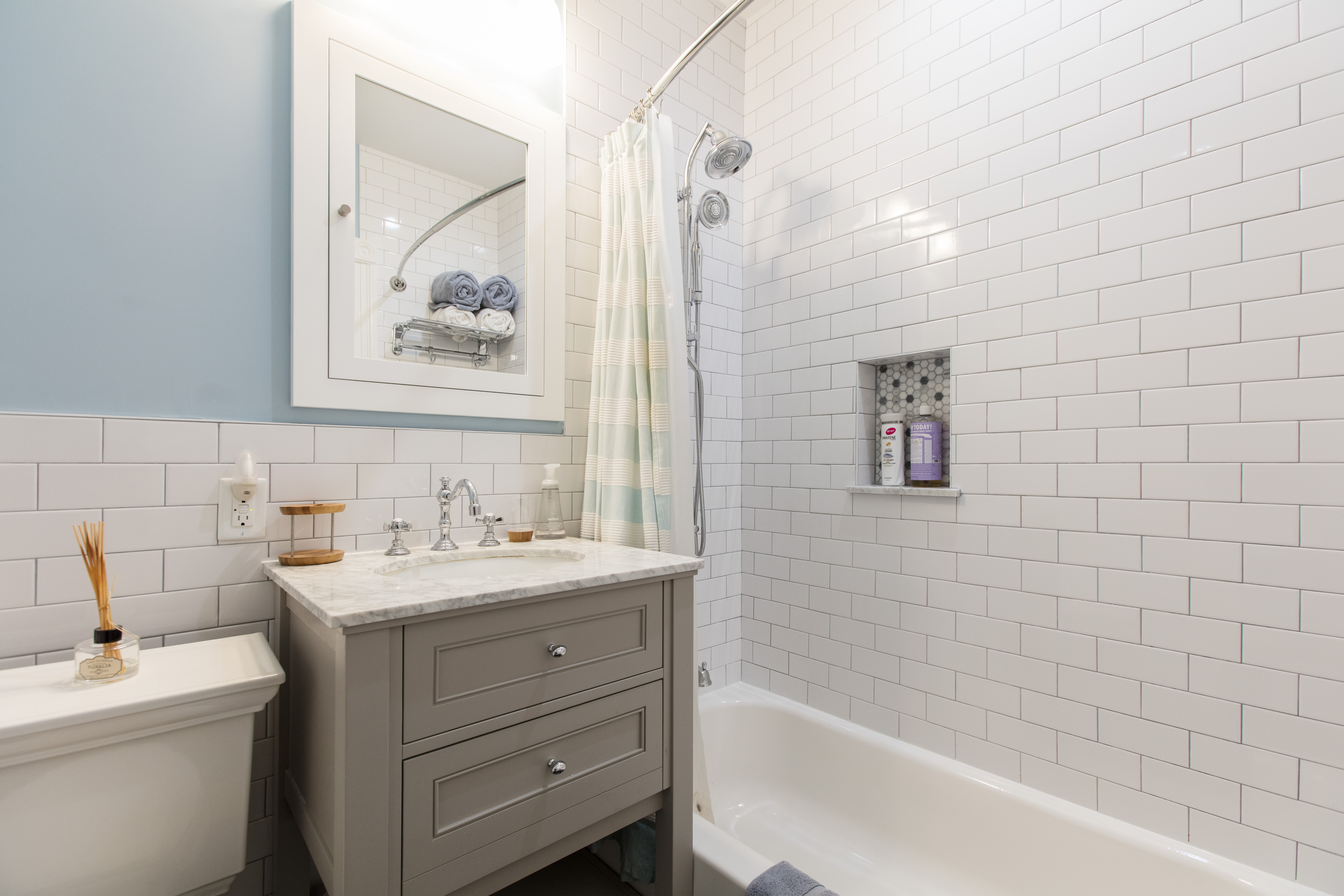 Park Slope brownstone remodel bathroom with white subway tile, gray vanity, tub and shower, recessed niche, blue walls, and polished chrome fixtures.