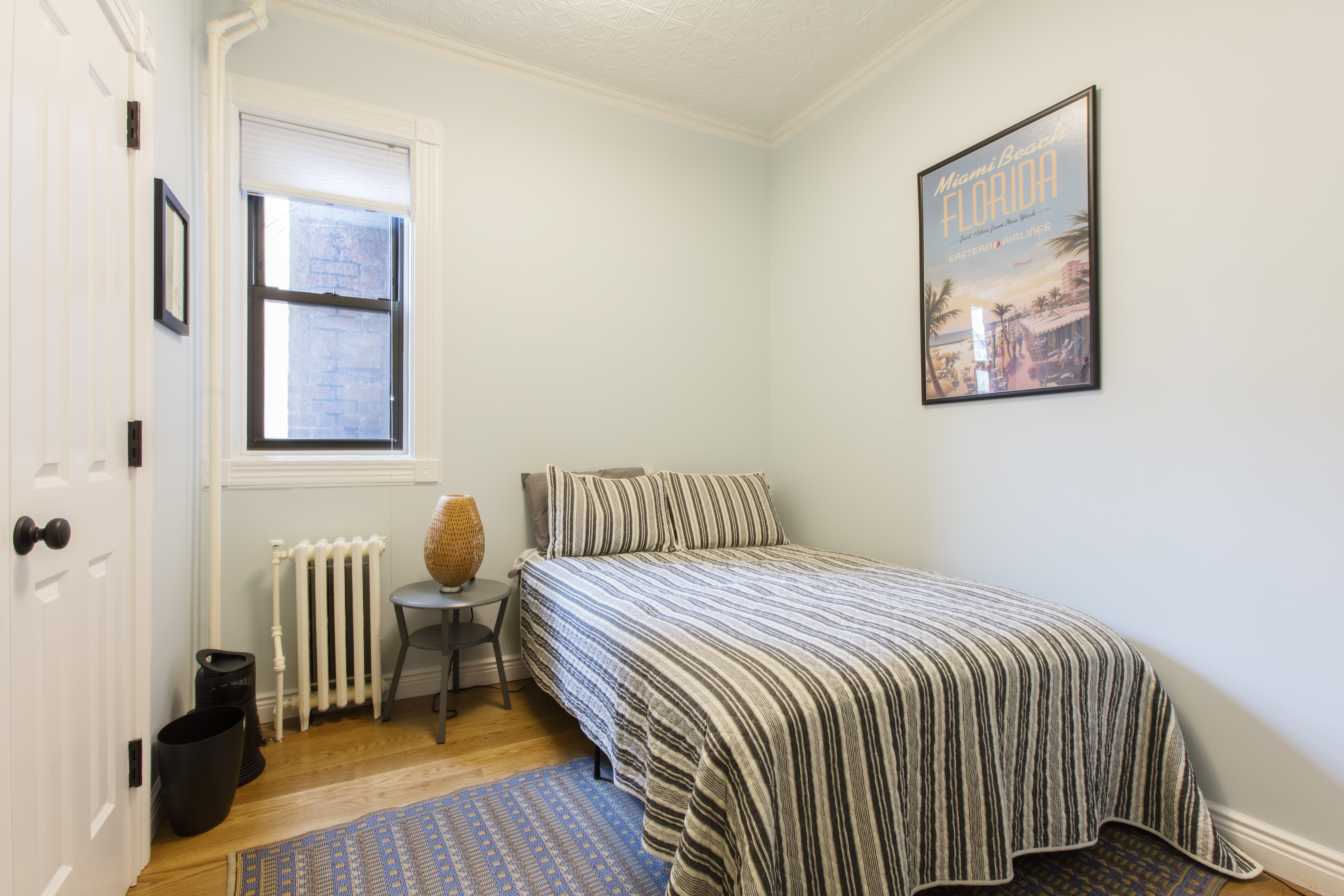 Park Slope brownstone remodel guest bedroom with a preserved tin ceiling, oak flooring, radiator, white trim, and a compact bed beside the window.