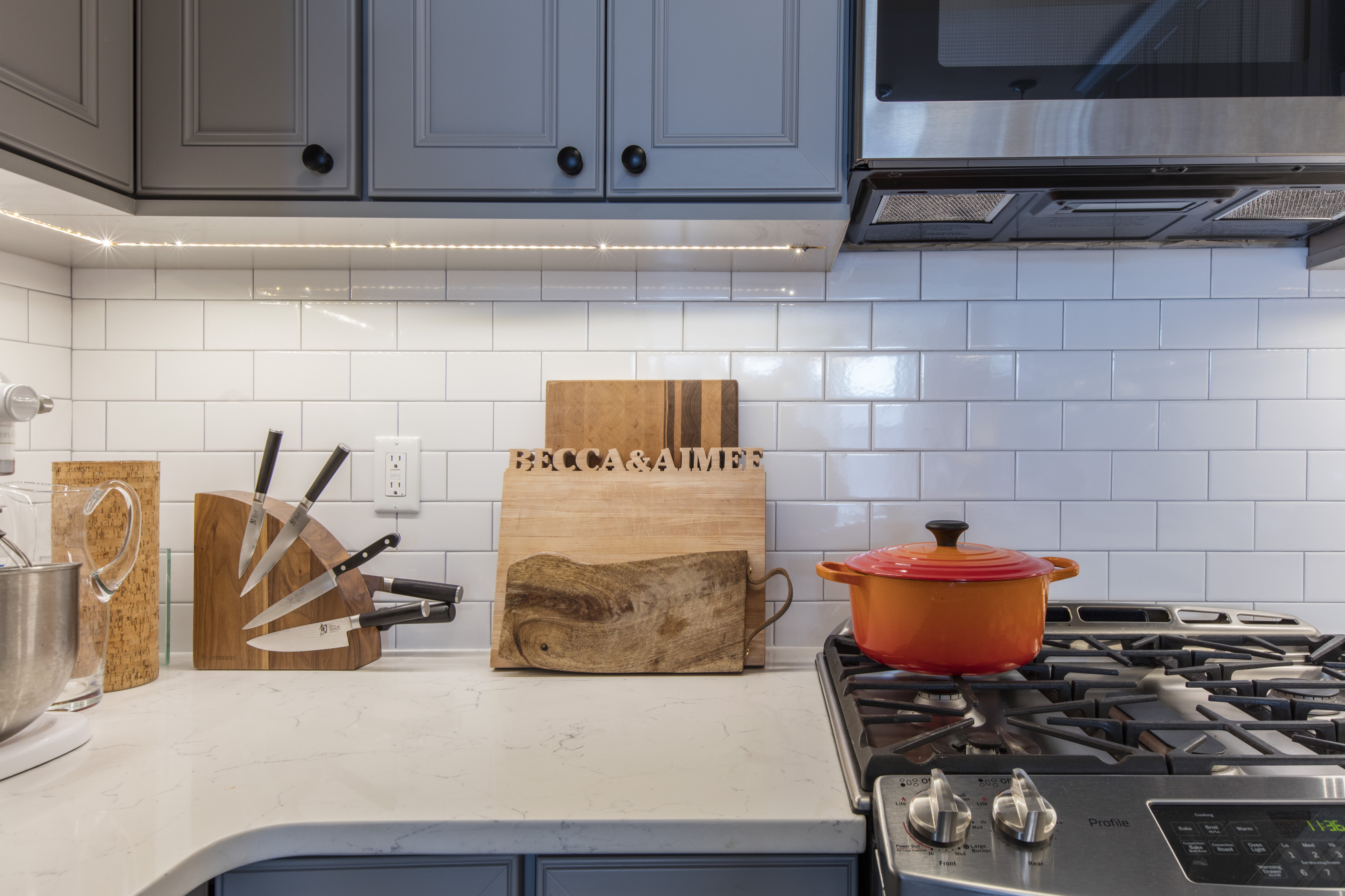Park Slope brownstone remodel kitchen detail with gray cabinetry, white subway tile, quartz countertop, stainless range, and under-cabinet lighting.