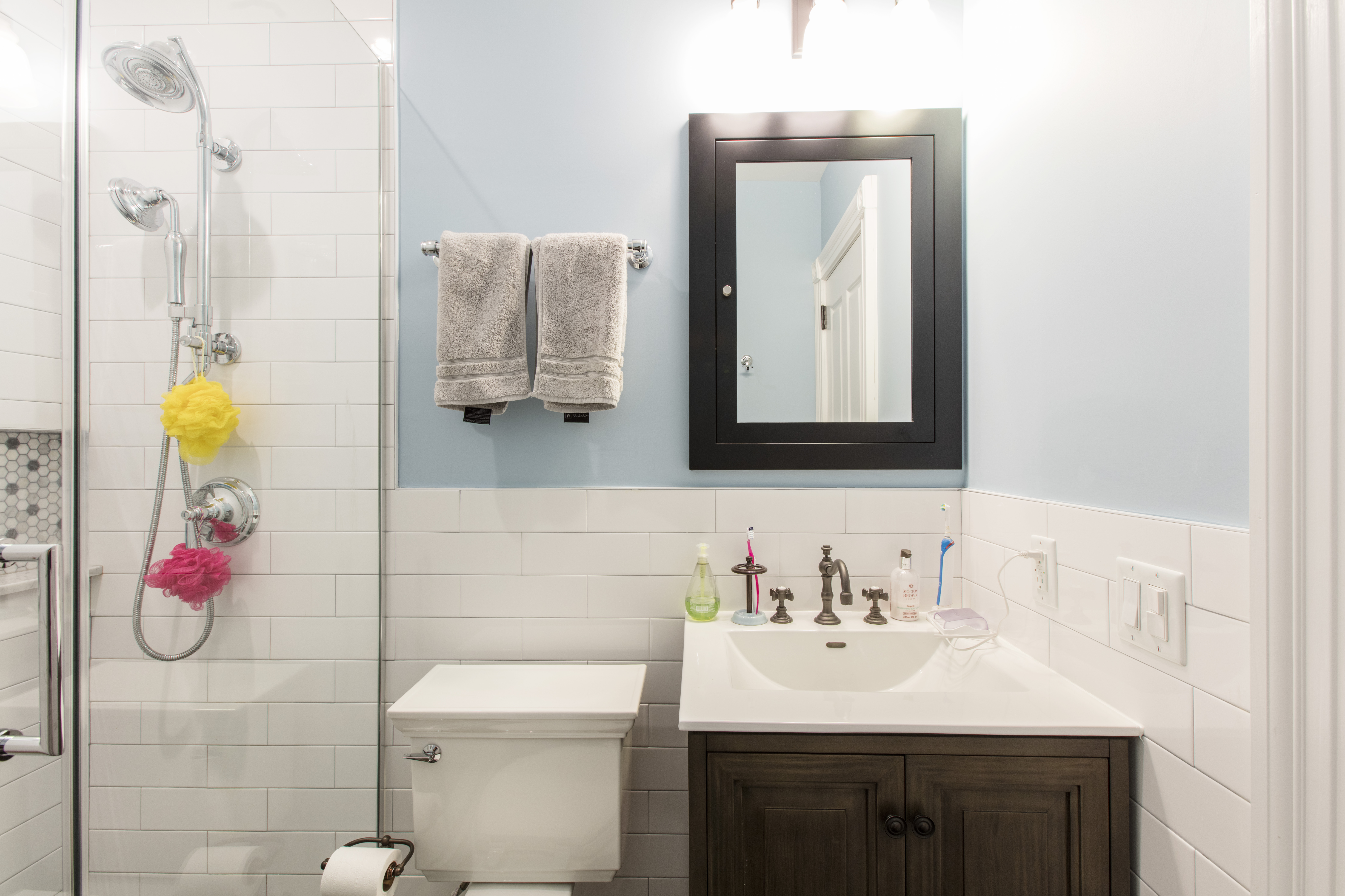 Park Slope brownstone remodel bathroom with white subway tile, glass shower enclosure, blue walls, dark wood vanity, and polished chrome fixtures.