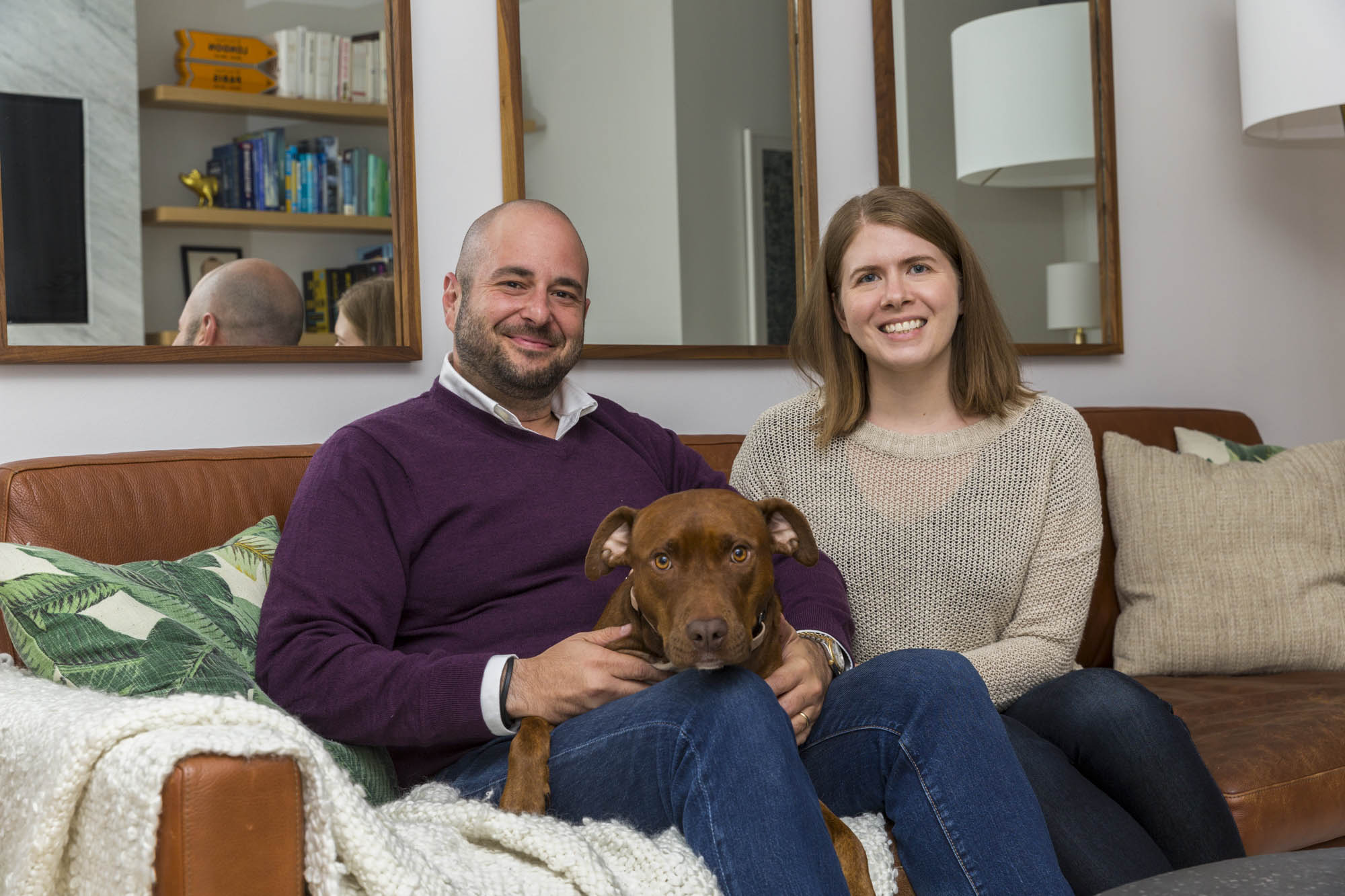 Homeowners sitting with their dog on brown sofa in renovated Manhattan living room.