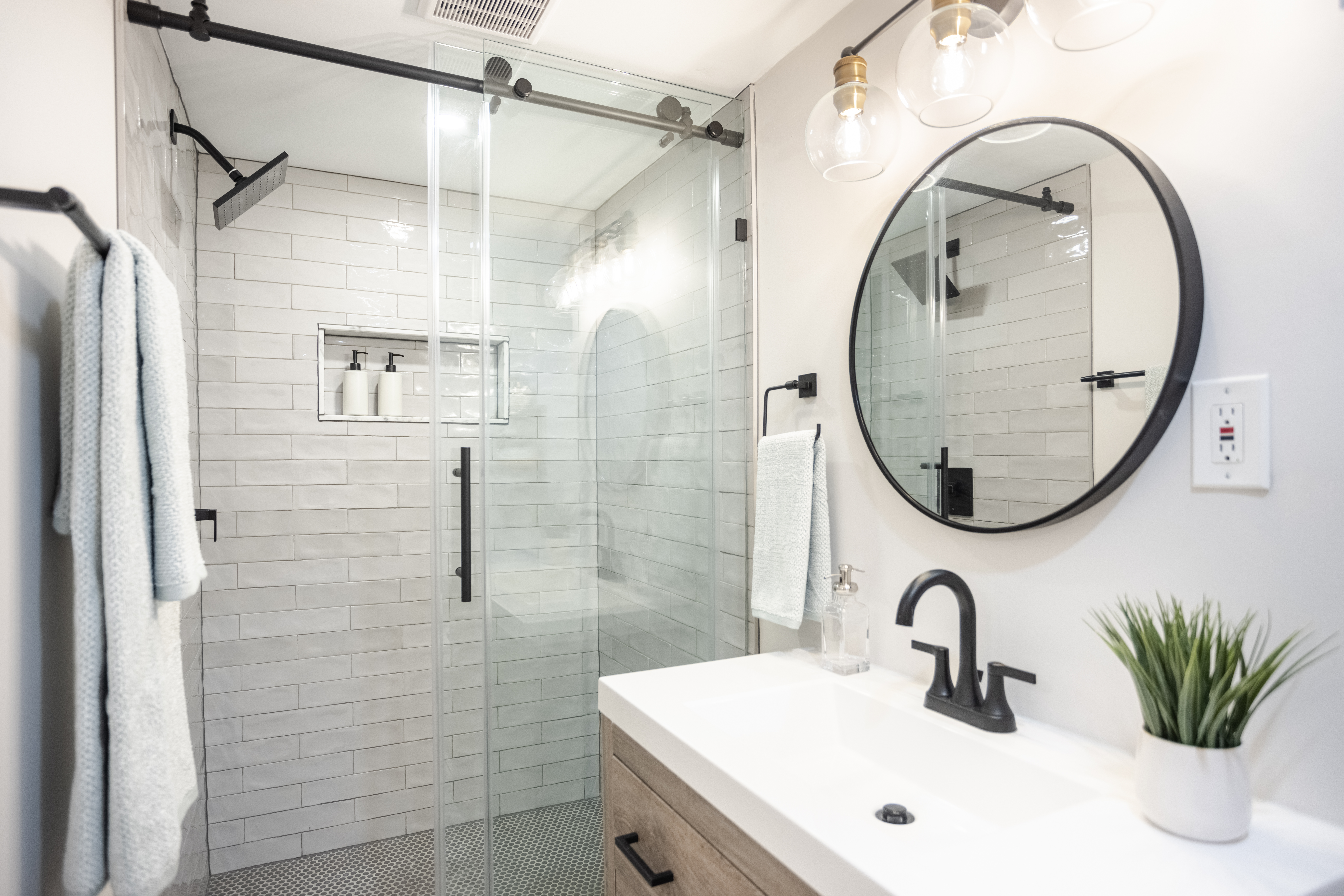 A sleek bathroom with a sliding glass shower door, white subway tiles, and a round mirror.