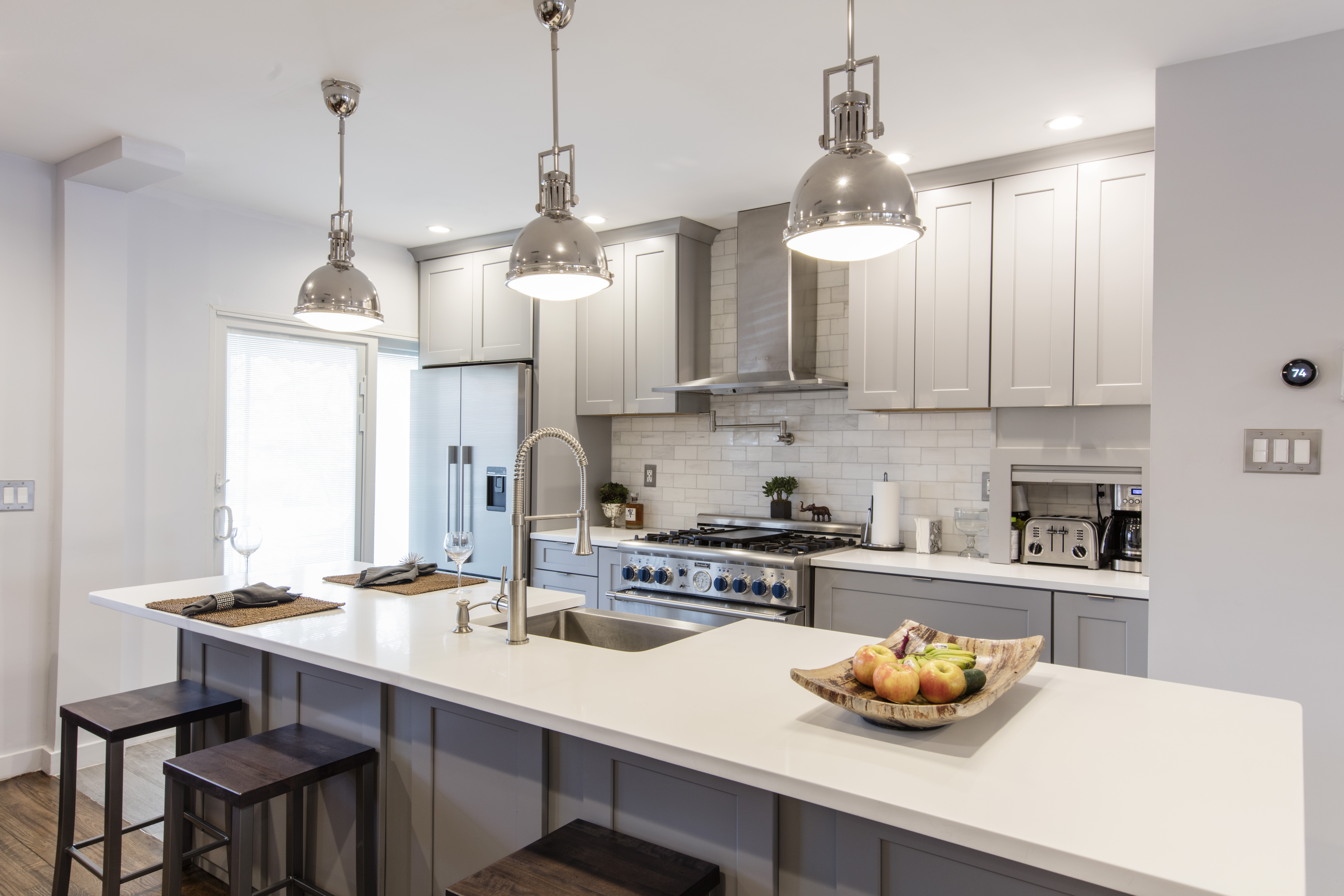 Modern kitchen with stainless steel appliances, gray cabinetry, and a white countertop, featuring pendant lighting over an island.