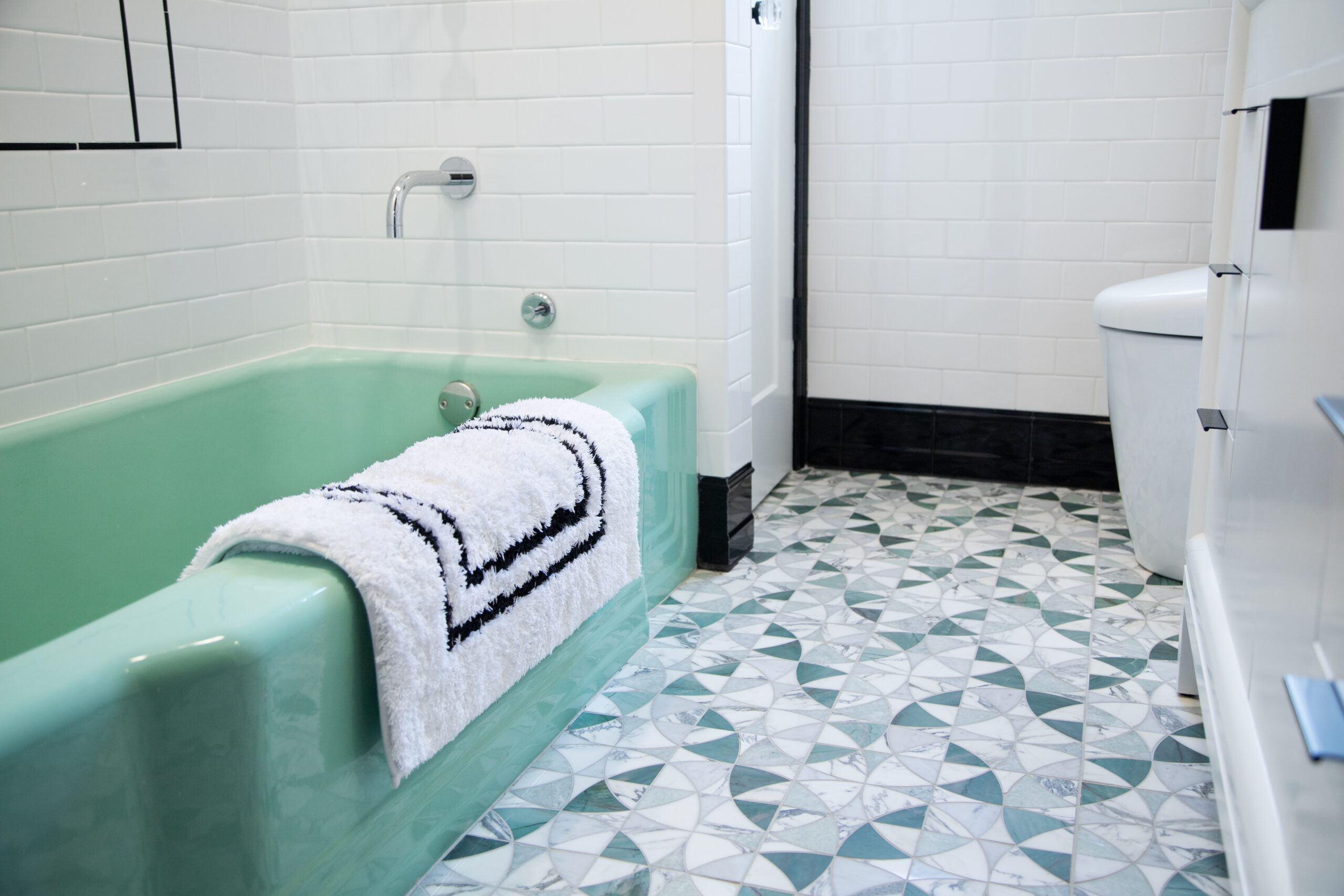 Green bathtub, patterned mosaic stone floor, and white subway tile in a vintage-meets-modern Jersey City bathroom remodel.