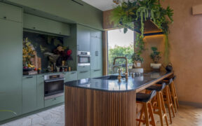Sage green cabinet color and warm wood textures pair with lush greenery for a dramatic, nature-inspired modern kitchen.