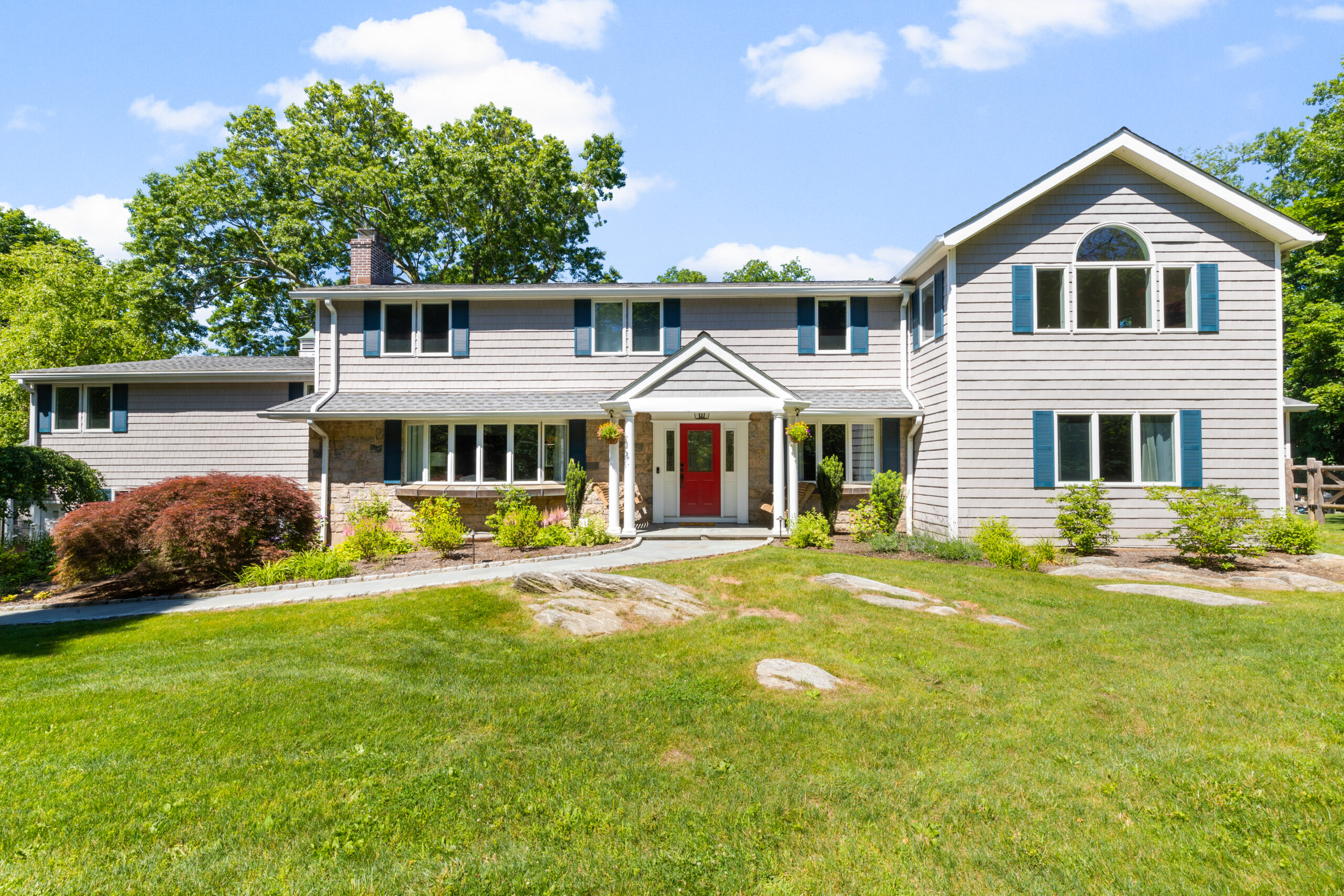 Front exterior of a house showing large windows, a paved pathway, and red front door.