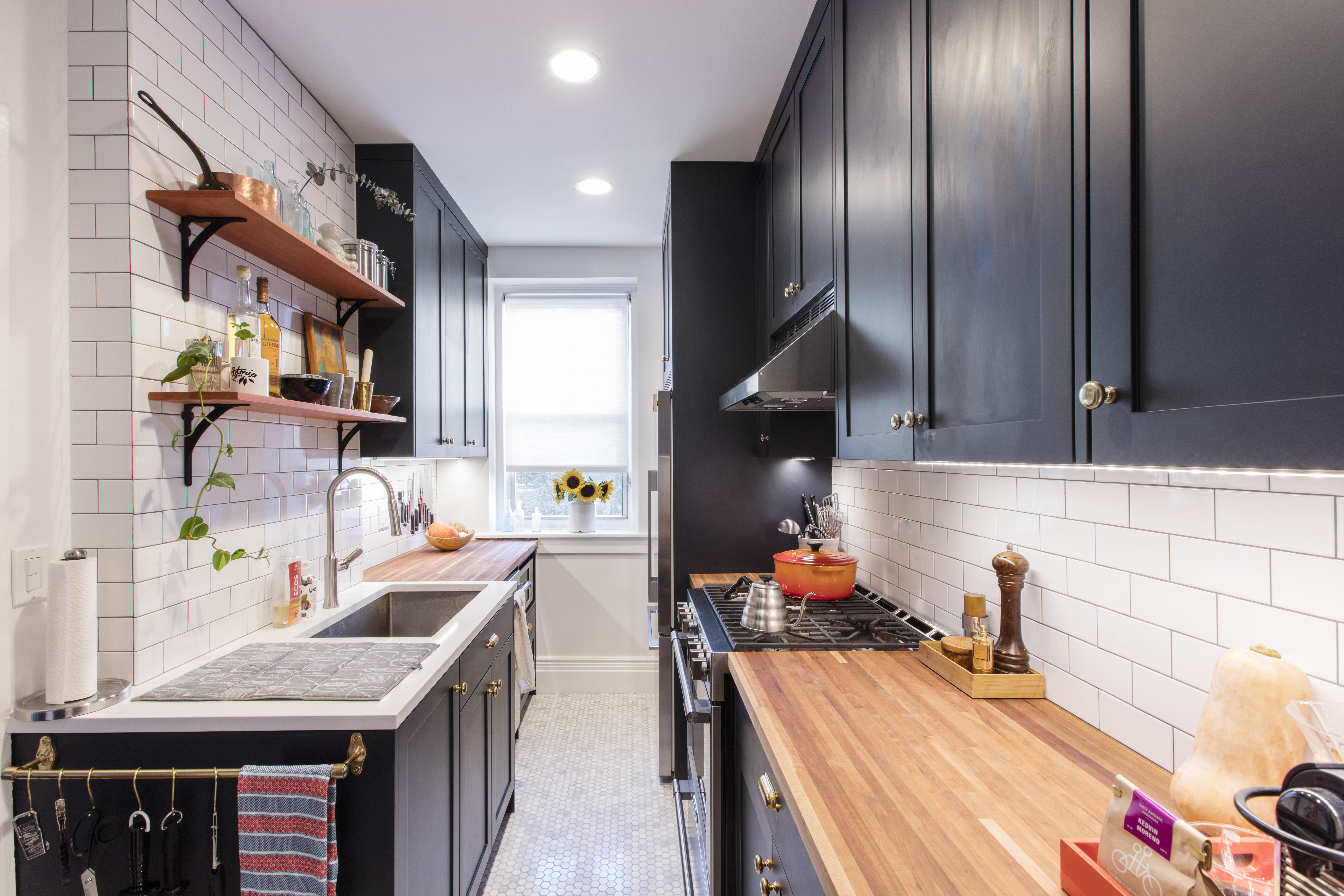 Narrow galley kitchen with dark cabinets, white subway tile walls and long butcher block countertops on both sides for prep and storage.