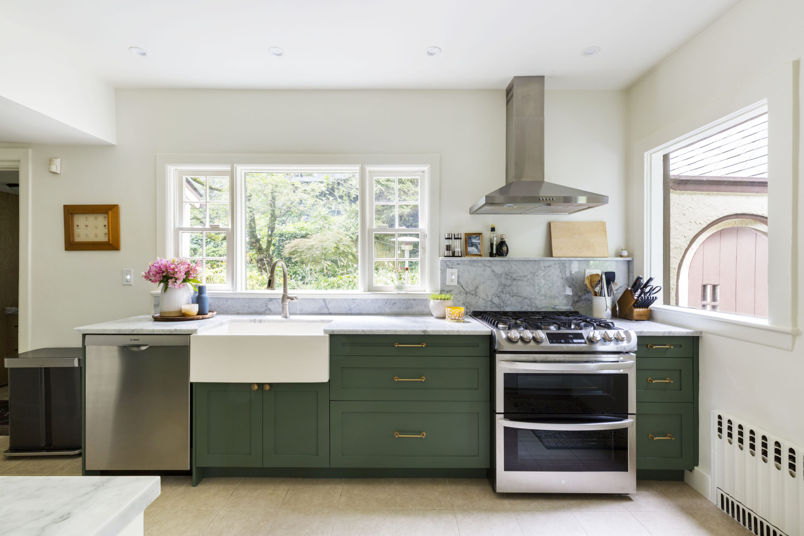 A bright kitchen with green lower cabinets, marble counters, and a farmhouse sink brings a fresh, classic look with garden views.