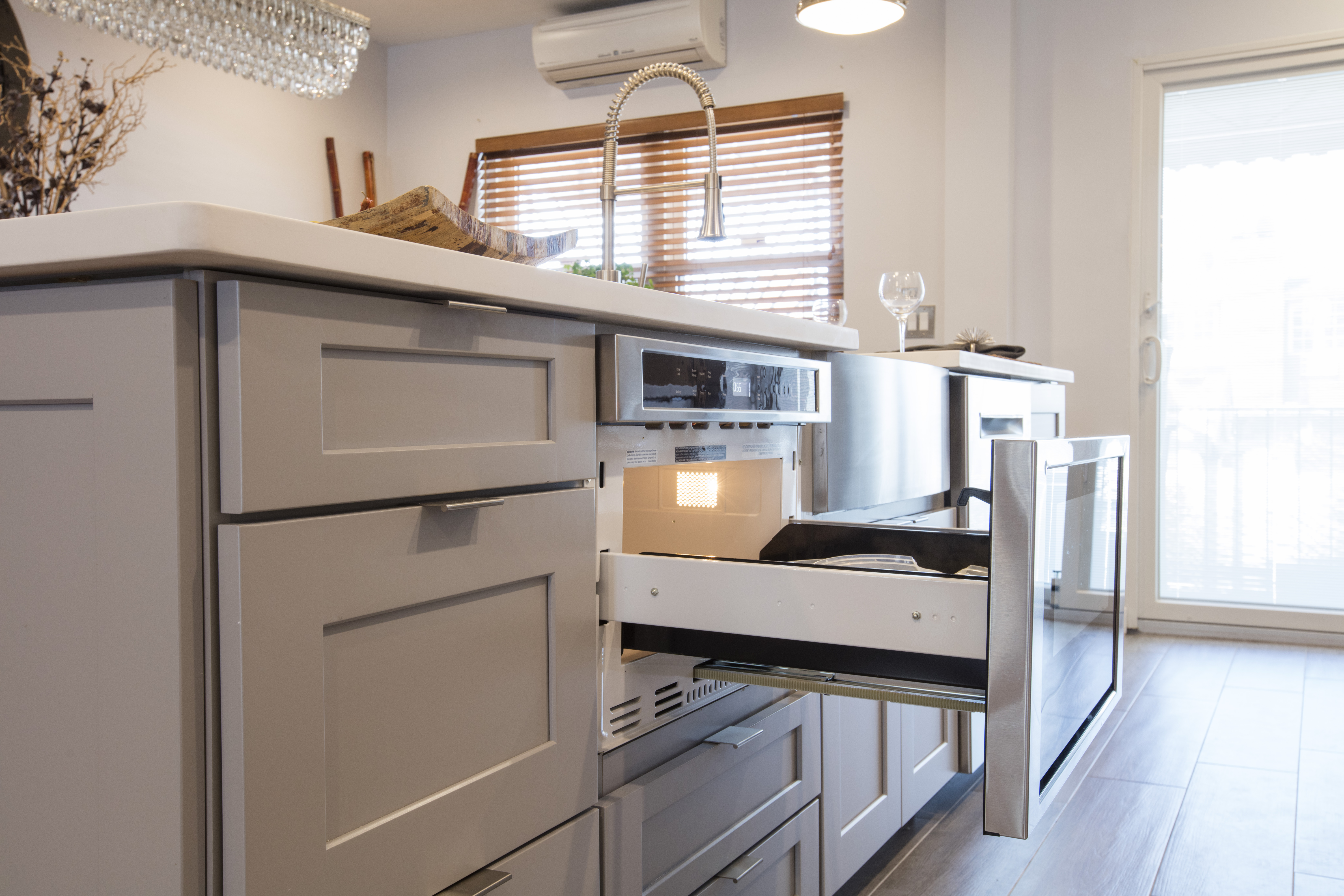 Close-up of gray island cabinetry with an open microwave drawer and wall oven, showing built-in appliances integrated into the peninsula.