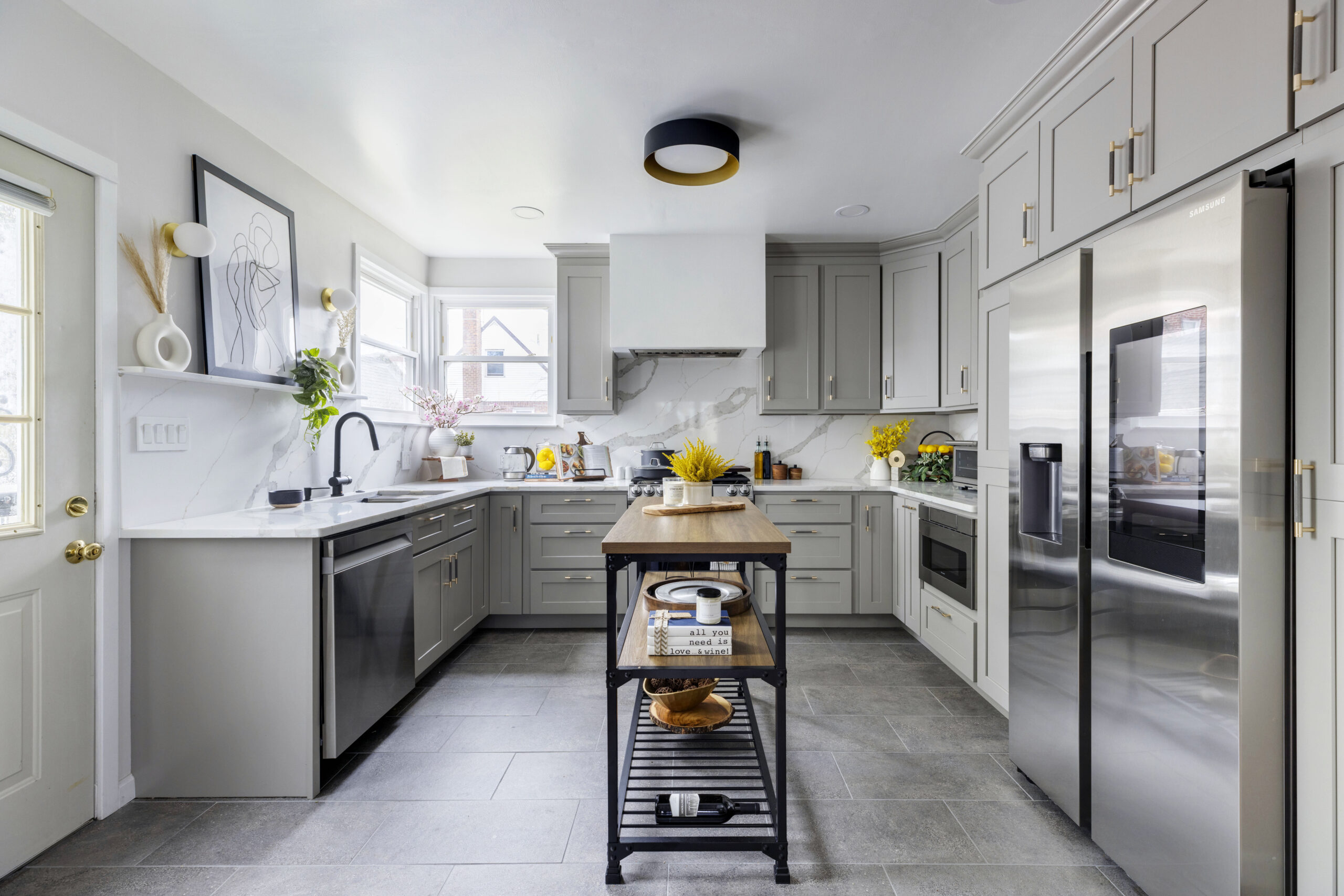Gray cabinet kitchen with marble backsplash, stainless appliances, and a narrow wood topped mobile island acting as a prep center.