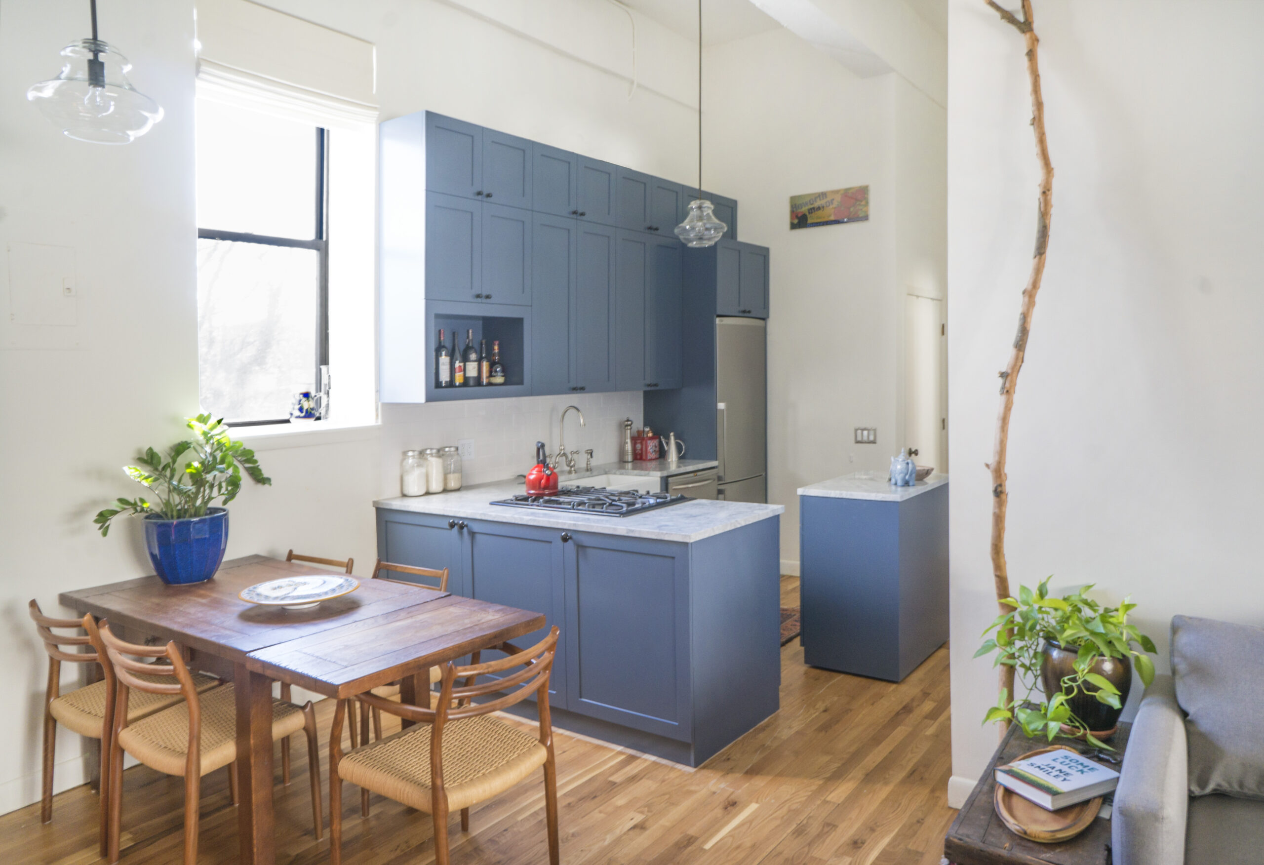 Cozy blue cabinet kitchen with marble counters, a small matching island at the back, and a wood dining table with woven chairs near the window.