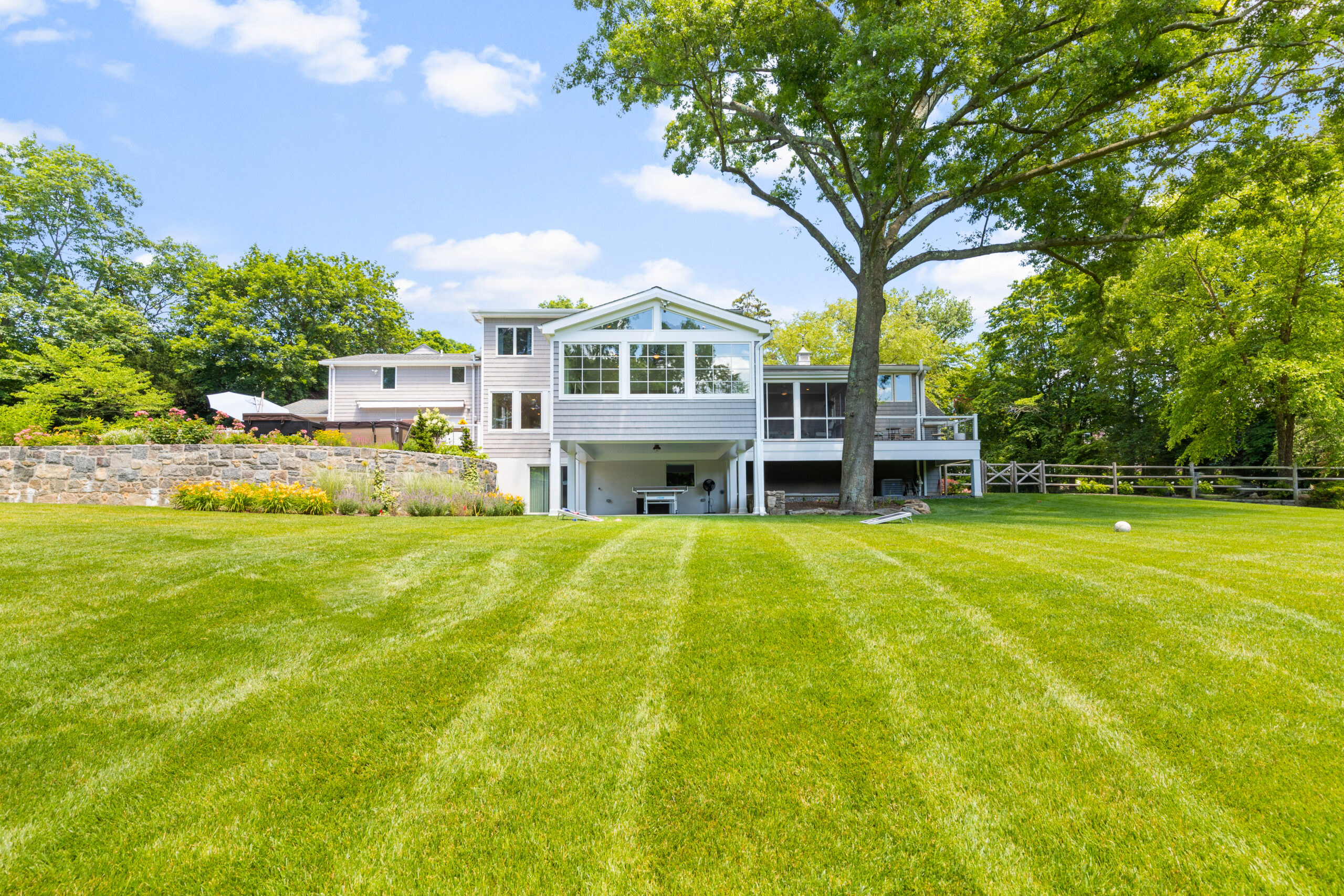 Rear exterior showing large windows, screened porch, stone wall, and expansive green lawn.