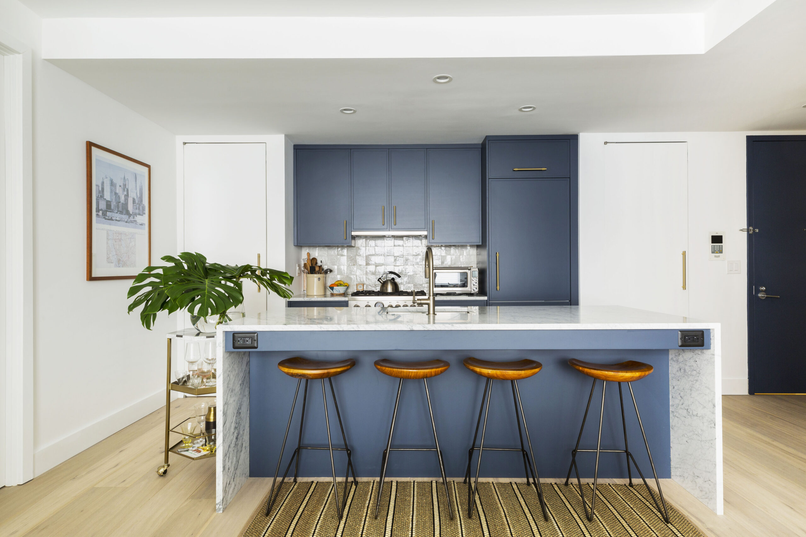 A sleek kitchen with slate blue cabinets, brass pulls, and a marble waterfall island blends modern lines with soft texture.
