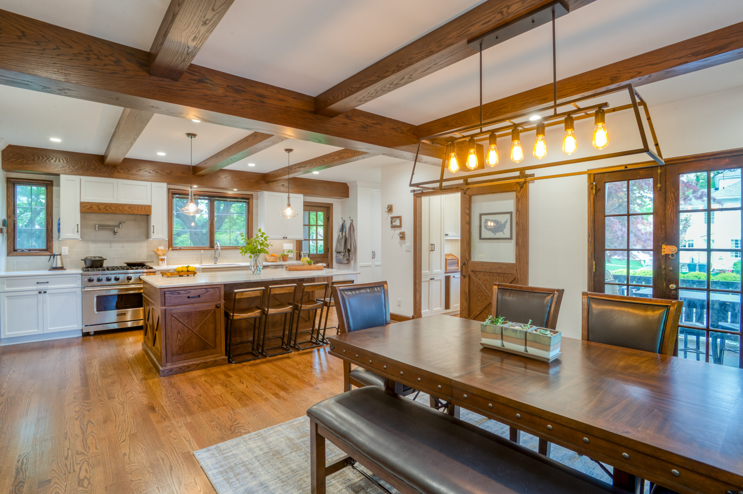 Open kitchen and dining room with oak beams, wood island, farmhouse table, leather chairs, and glass doors bringing in garden views.