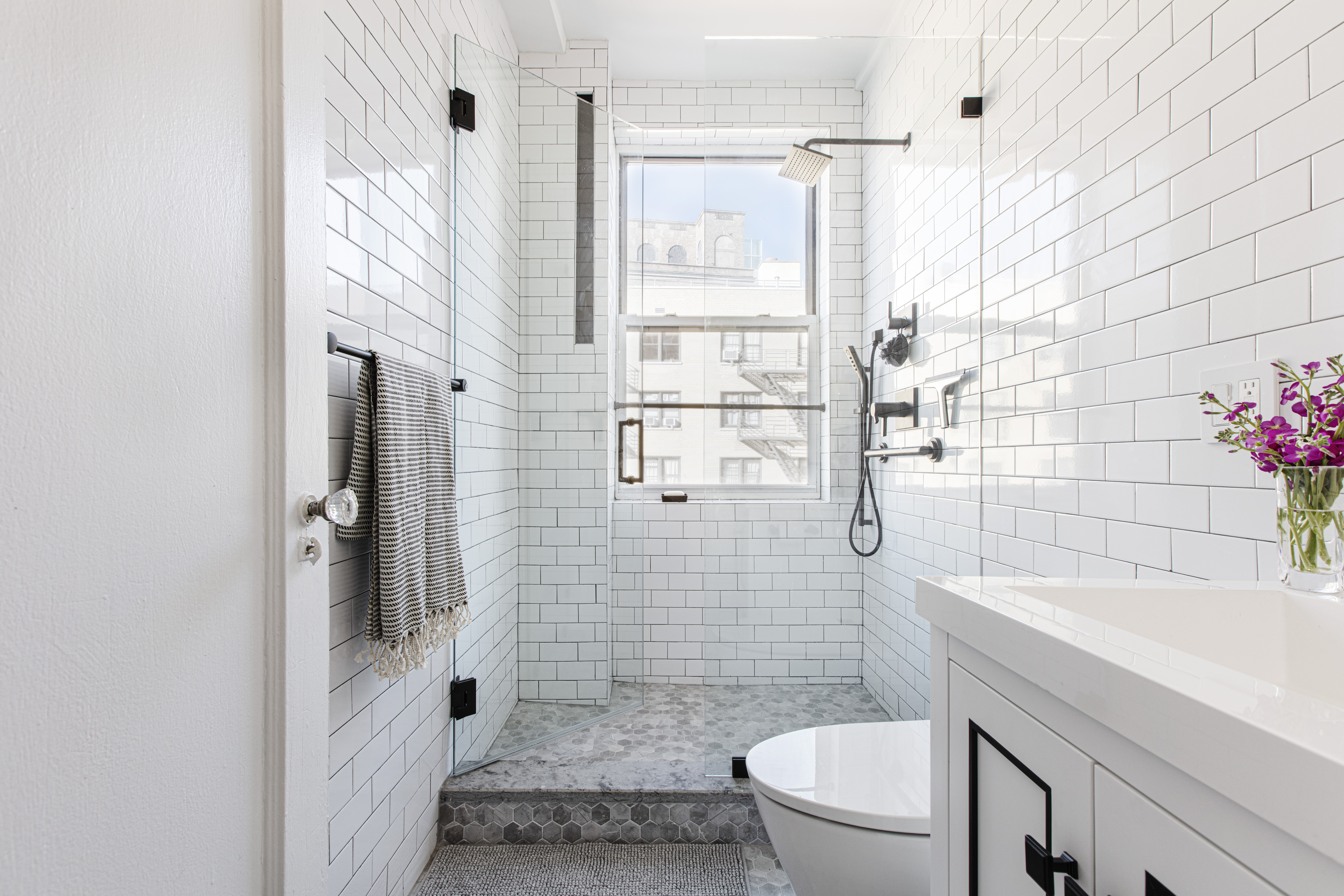 White subway tile bathroom with windowed walk-in shower, hex tile floor, glass panels, and black hardware accents.