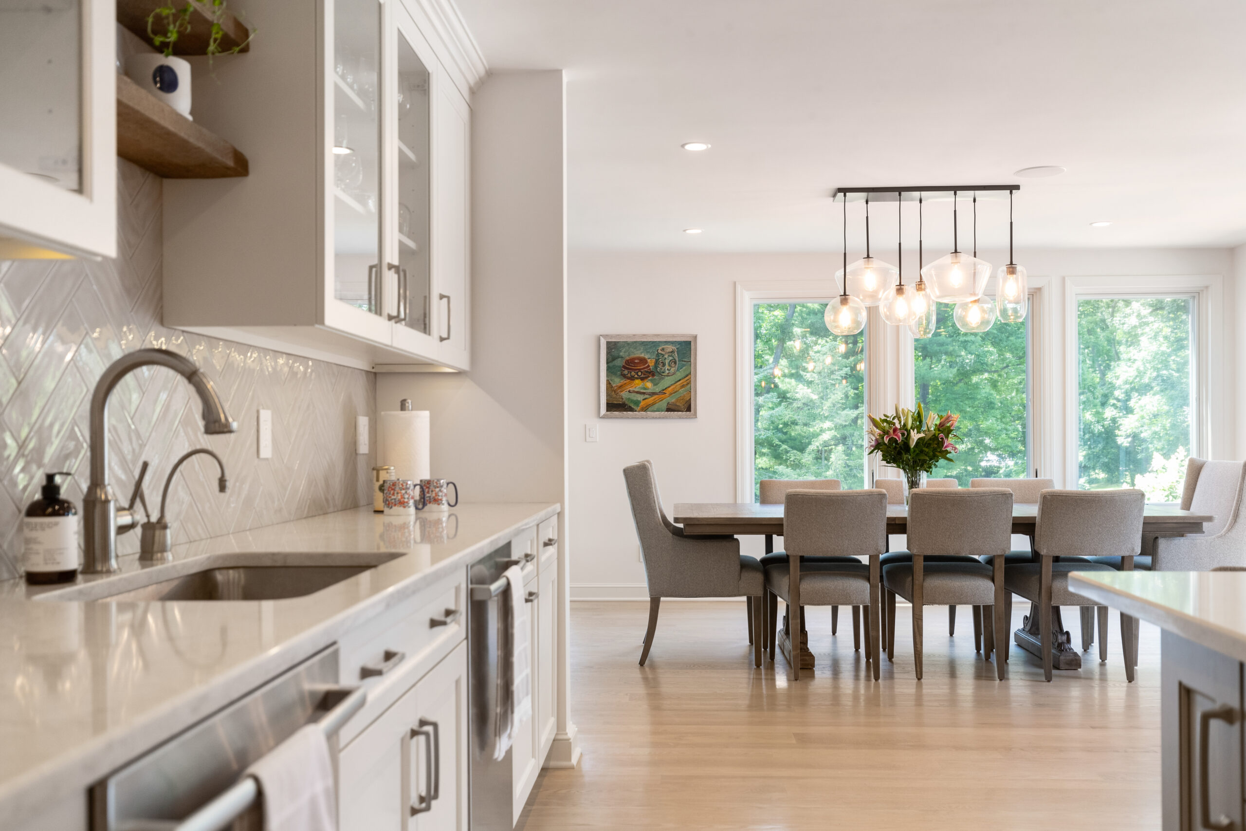 Kitchen and dining area with white cabinets, herringbone backsplash, and pendant lighting with outside view.