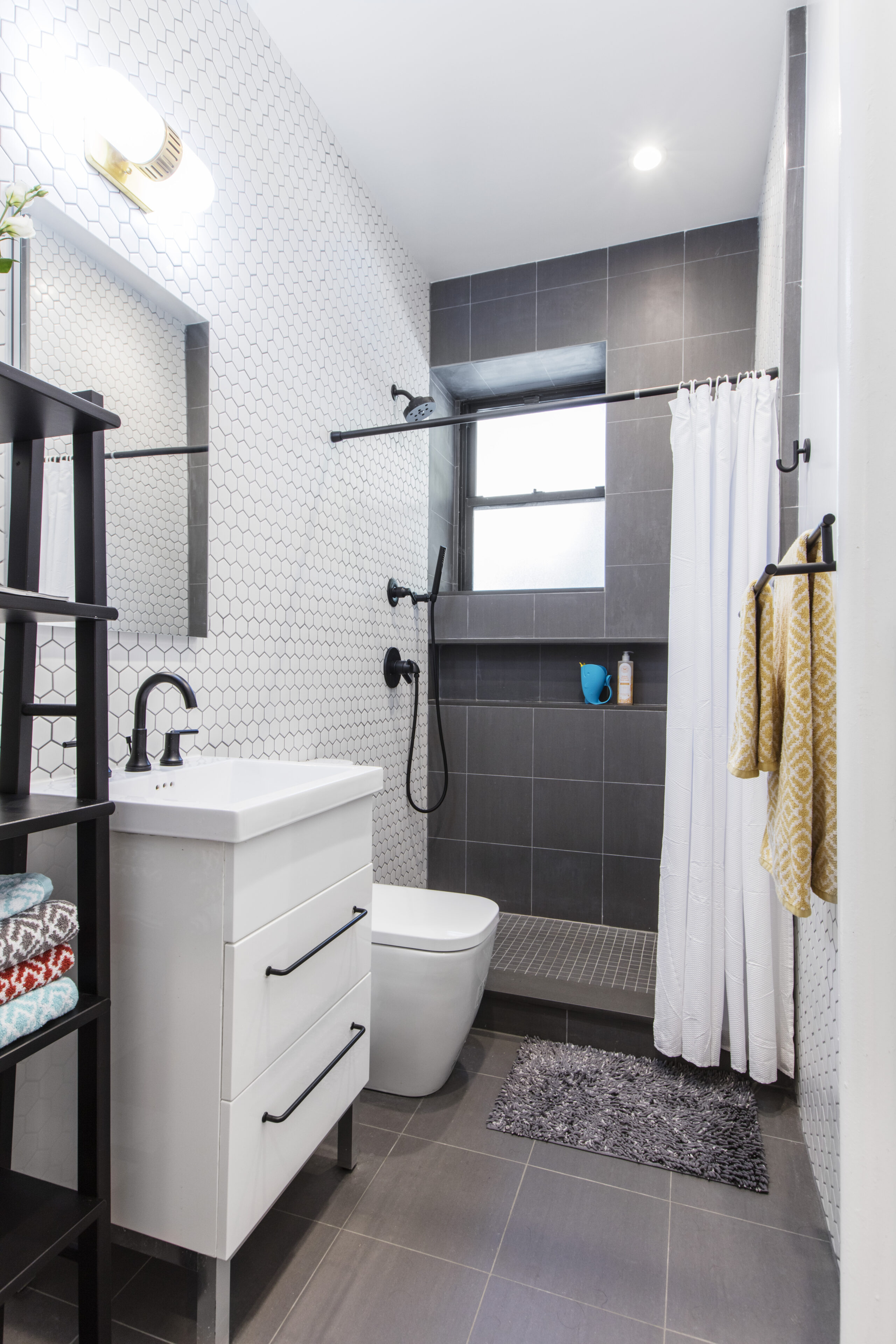 Compact bath with hex wall tiles, gray floor, walk-in shower with low step, and matte black fixtures.