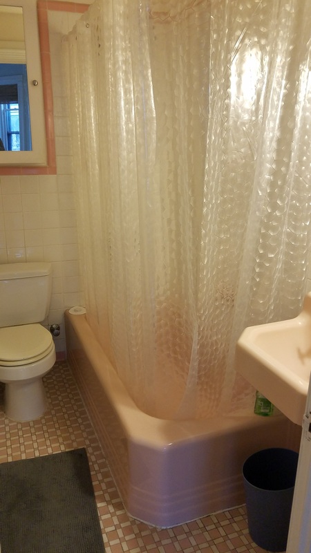 Old bathtub with curtains, toilet, and vanity prior to a tub to shower conversion.