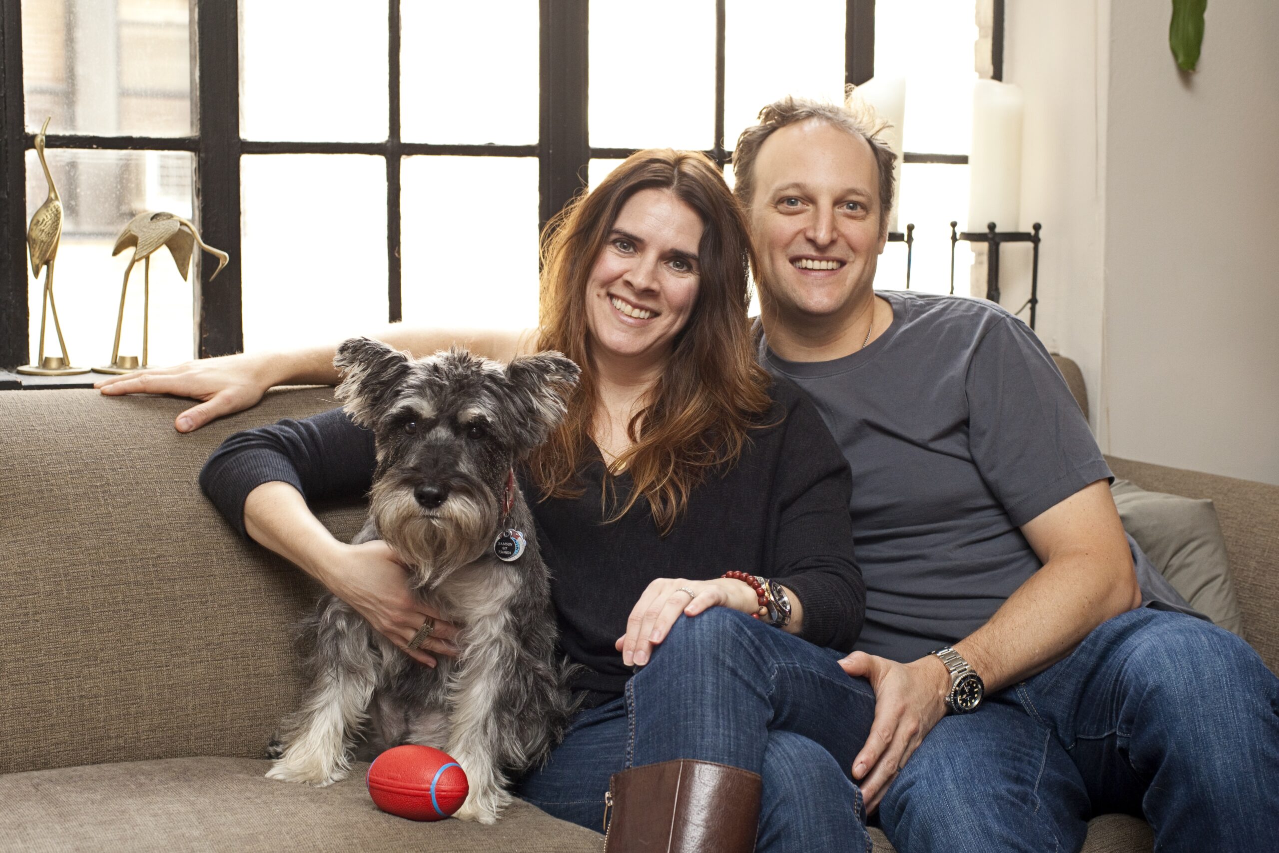Couple sitting on sofa with their dog in a bright Murray Hill apartment after bathroom remodel.