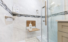 Walk in shower with fold down seat, grab bar, handheld spray, and slip resistant tile floor designed as a safe, elderly friendly bathing space.