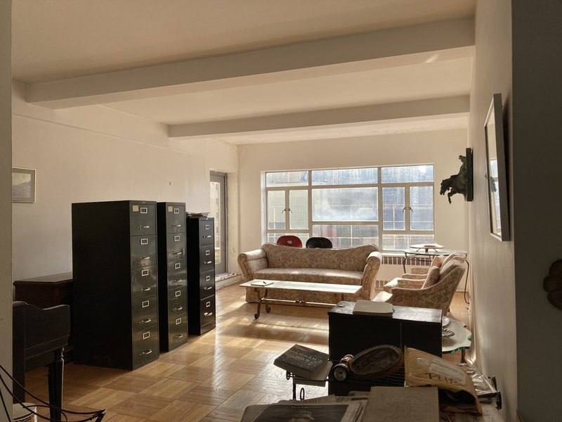 Before view of the Upper West Side penthouse living room, with dated furniture, file cabinets, and low natural light prior to the renovation.