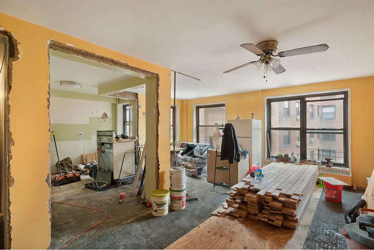 A mid-renovation apartment interior showing open walls, stacked flooring, and construction tools in progress.