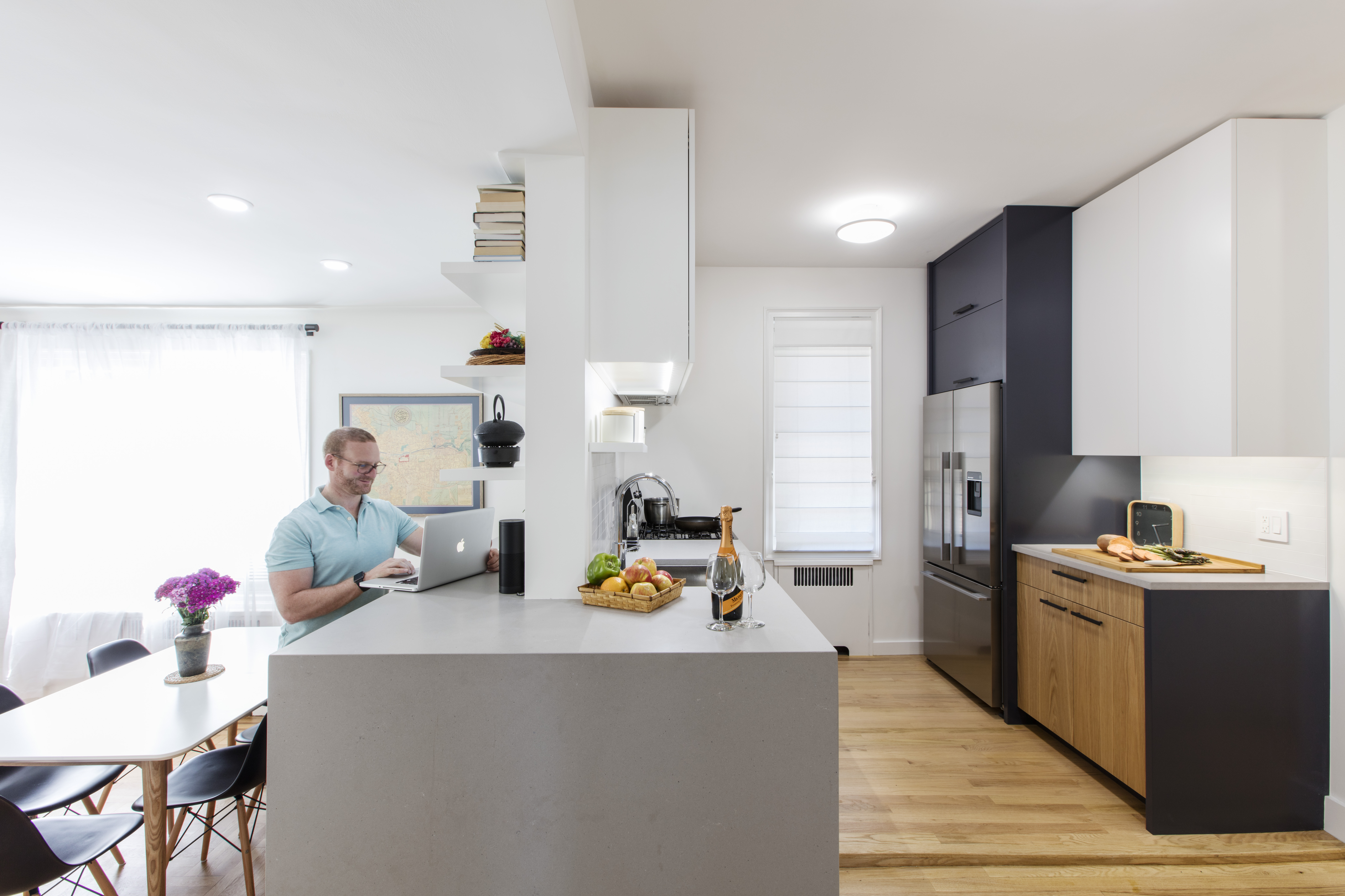 A homeowner works on a laptop in a newly remodeled kitchen with white cabinets and light wood floors.