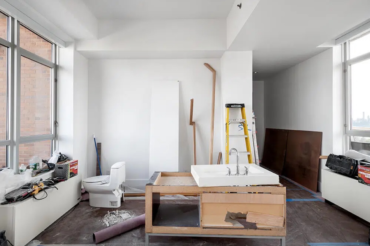 A partially completed high-rise apartment bathroom under renovation with tools, ladders, and new fixtures.