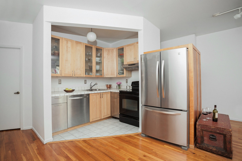 Before image of a small, boxed-in kitchen with wooden cabinets and flooring