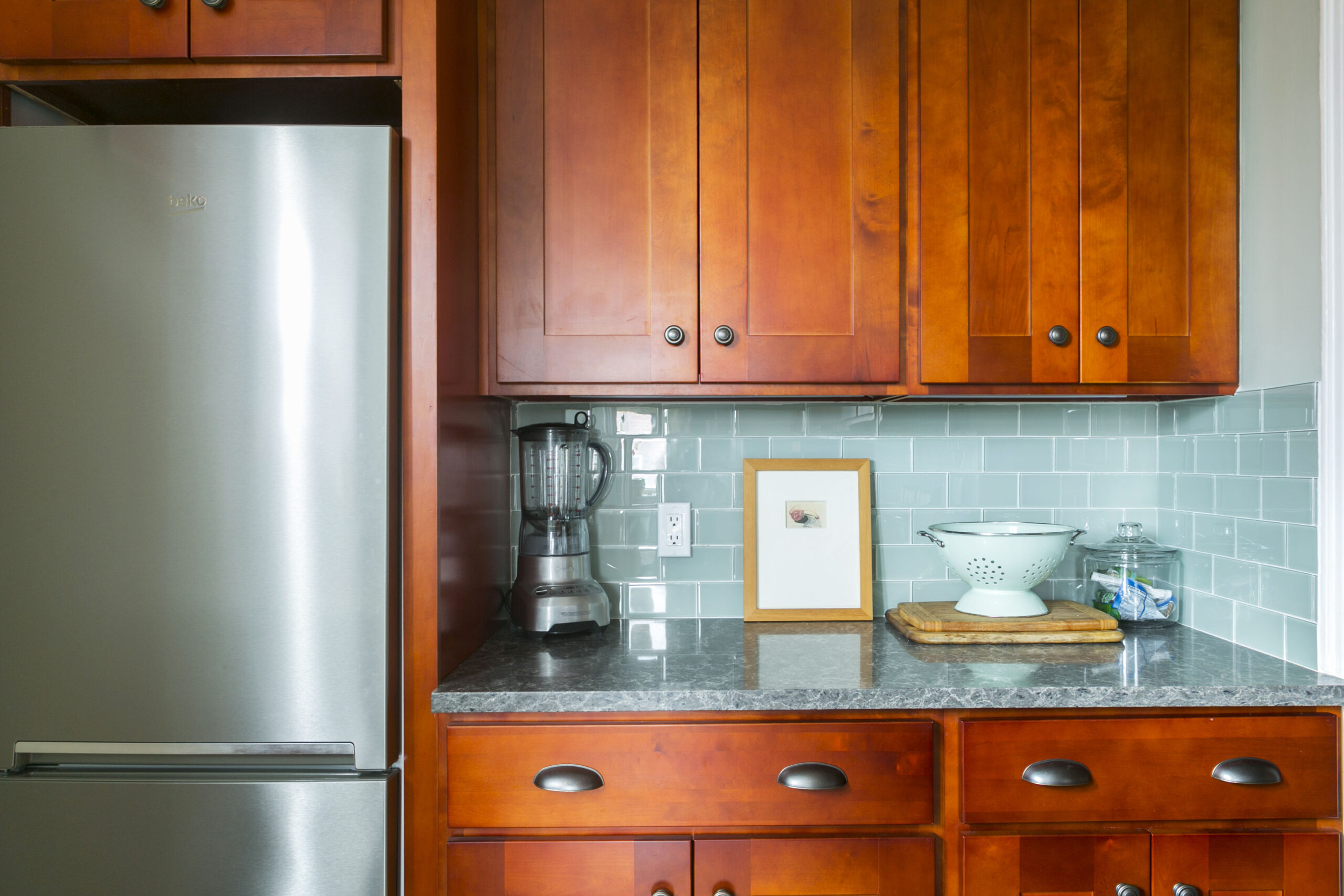 Kitchen with wood-stained cabinets, green backsplash, and quartz slab countertop