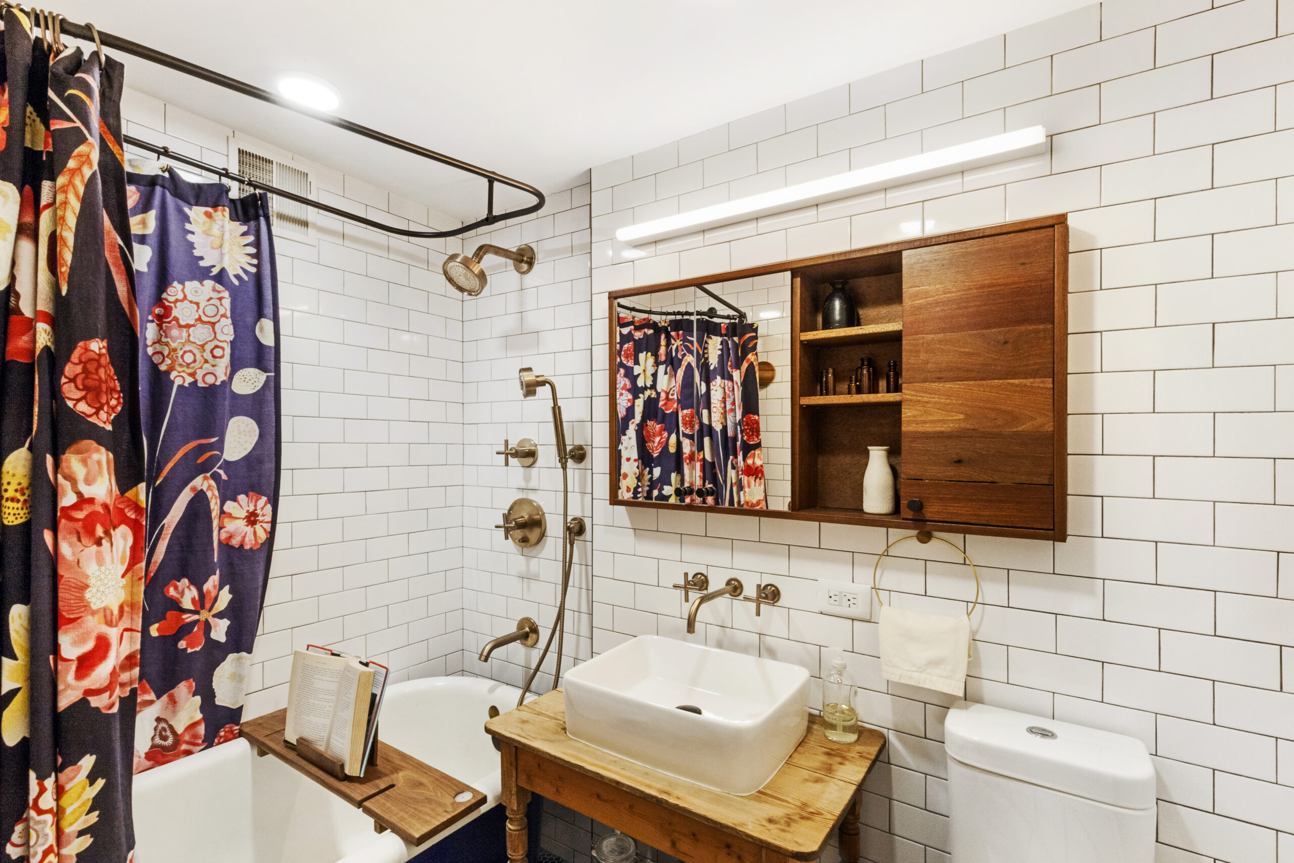 A renovated bath featuring a table-style bathroom vanity, vessel sink, wall spout, and white subway tile.