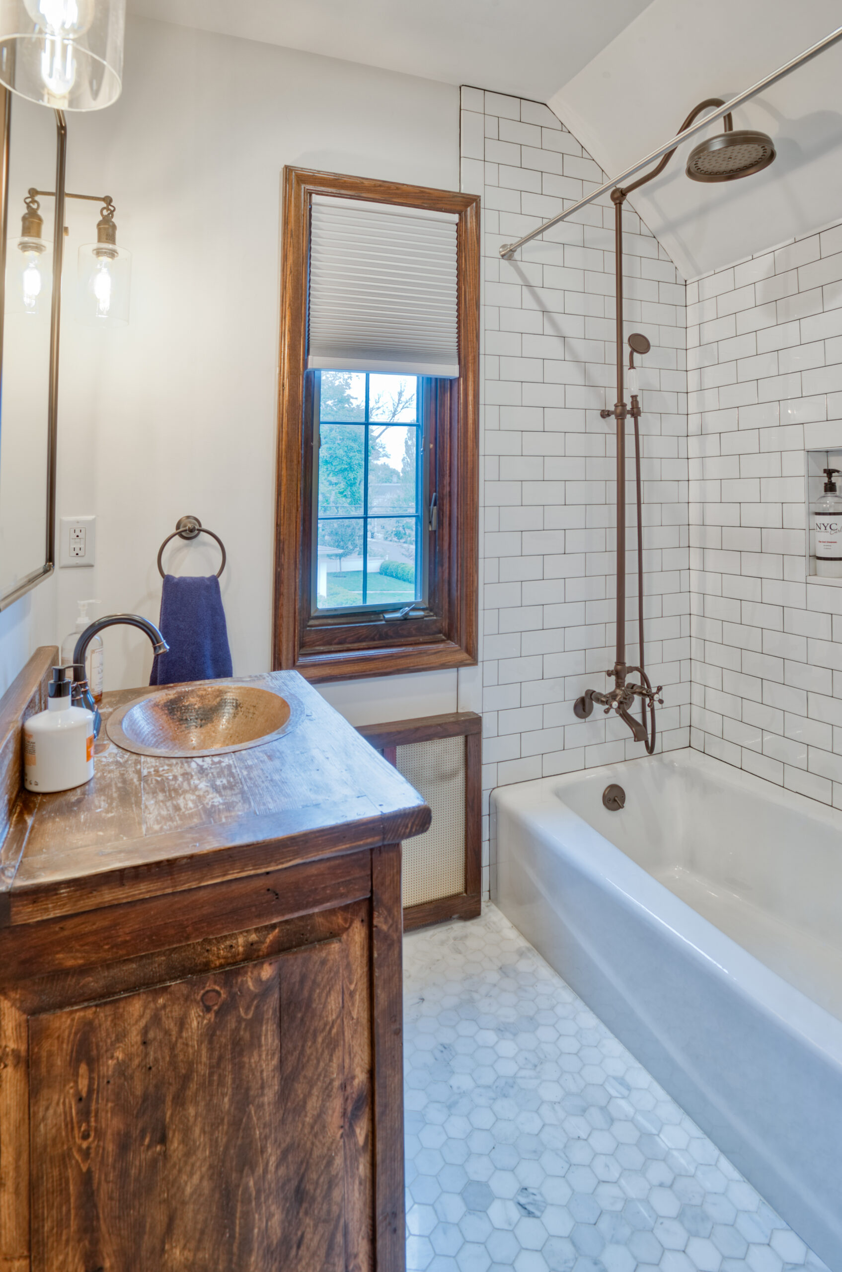 A bath remodel with a reclaimed-wood bathroom vanity, hammered copper bowl sink, and subway tile surround.