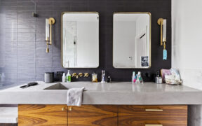 A bathroom featuring black statement wall tile, brass fixtures, vanity with wood cabinetry and drawers