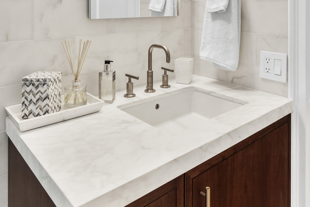A Calacatta marble vanity countertop with wooden cabinetry and brass faucet