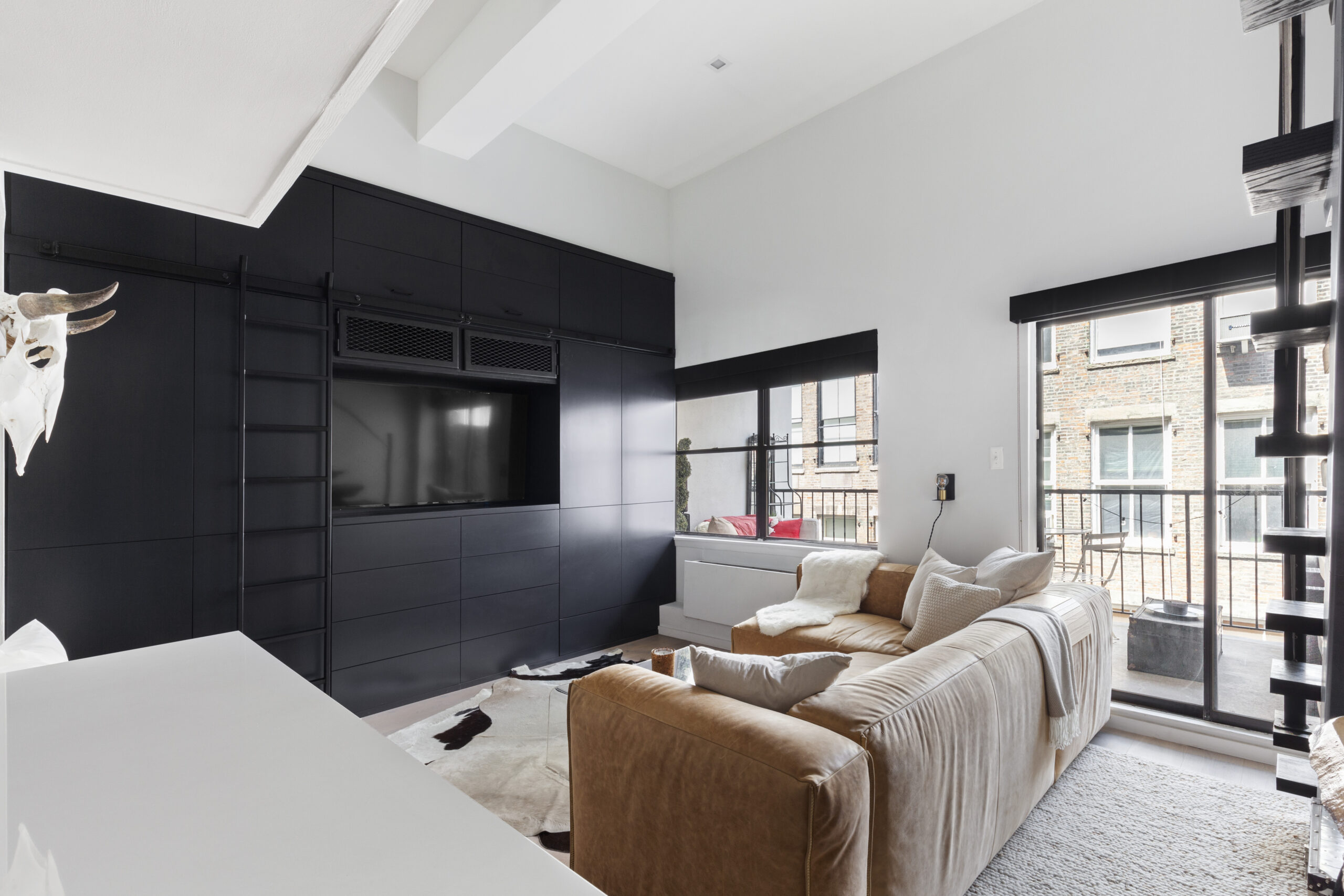 Studio loft in Manhattan featuring a leather couch in living room with TV screen and black drawers with a balcony