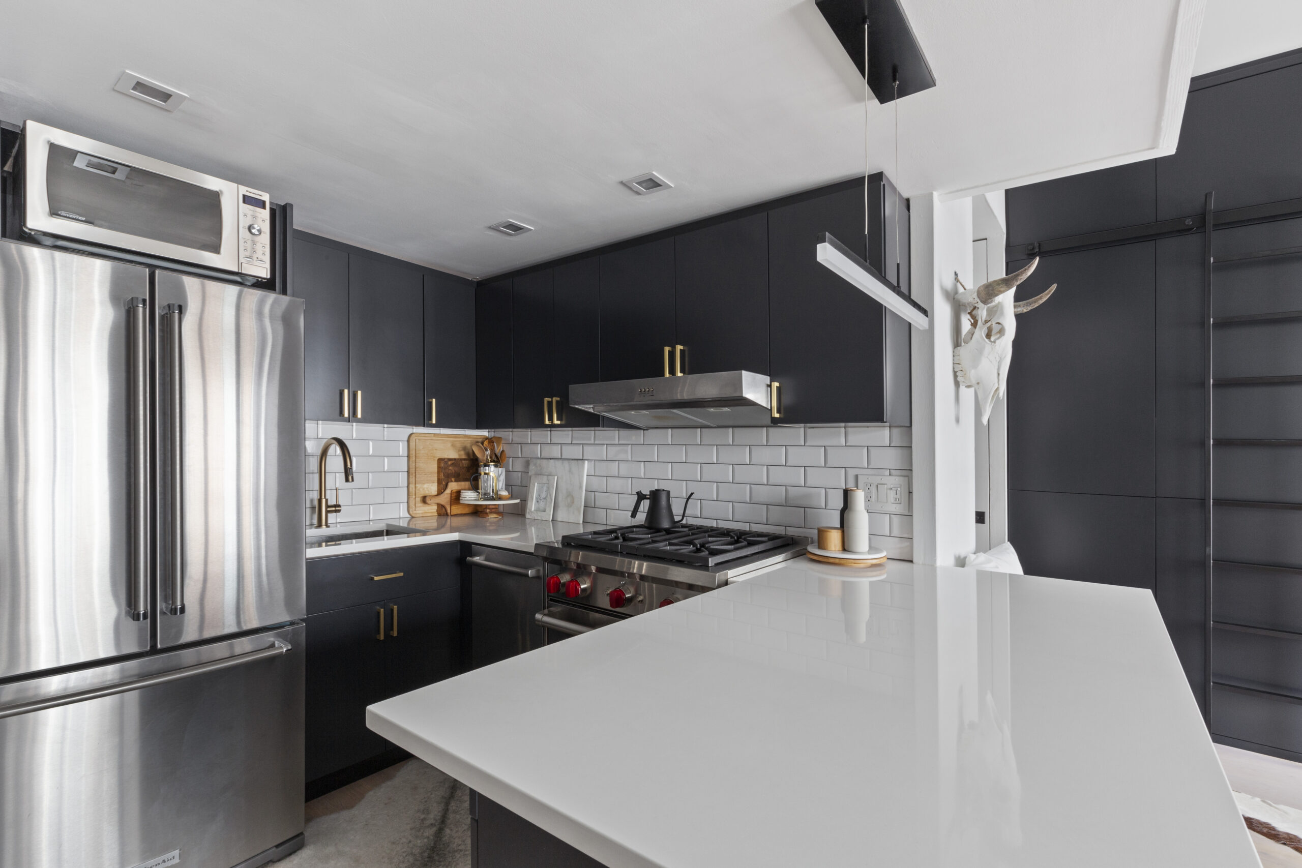 Renovated kitchen of a studio loft in NYC with white subway tile backsplash, kitchen peninsula, and black cabinetry