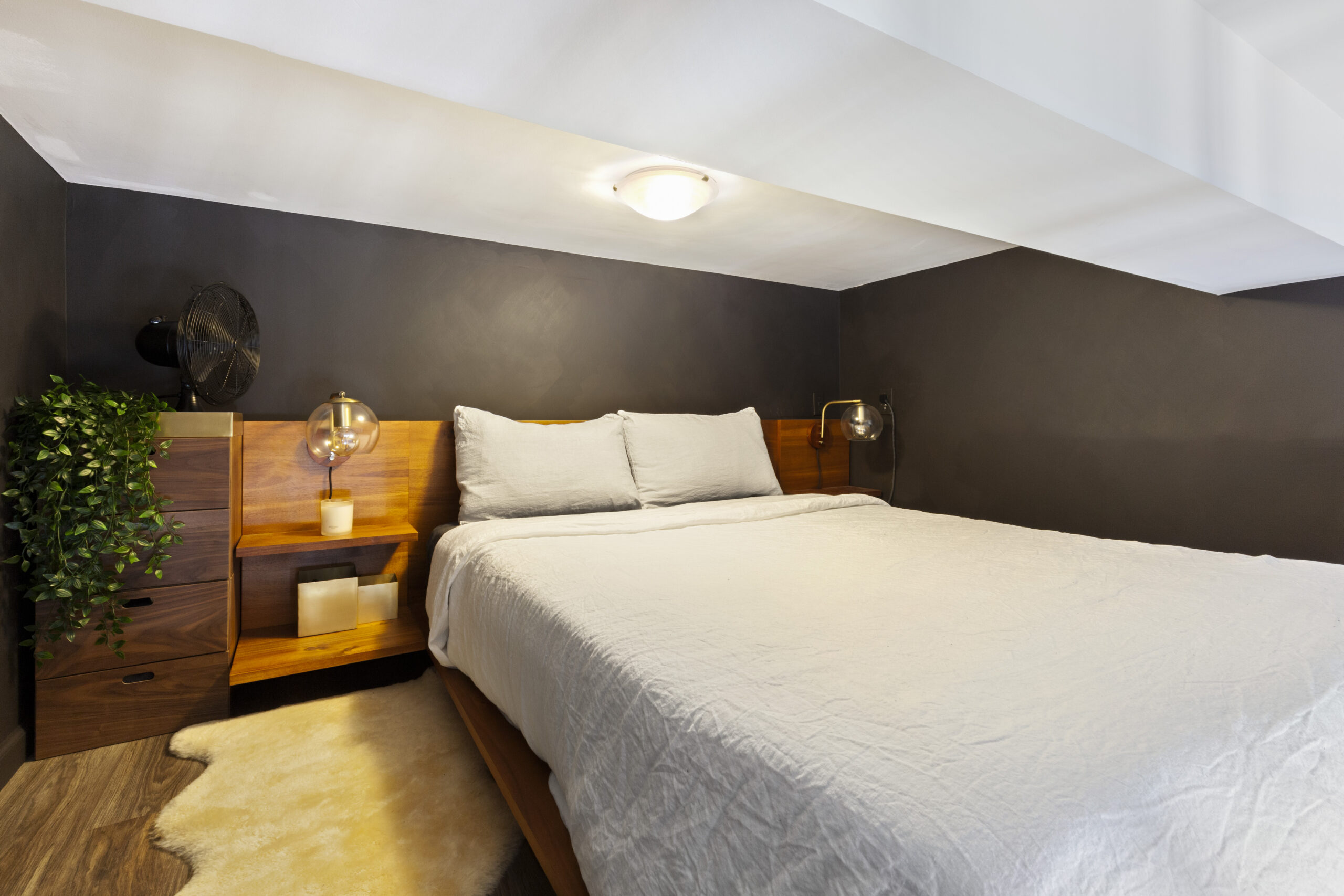 A studio loft bedroom with warm lighting and wooden side tables